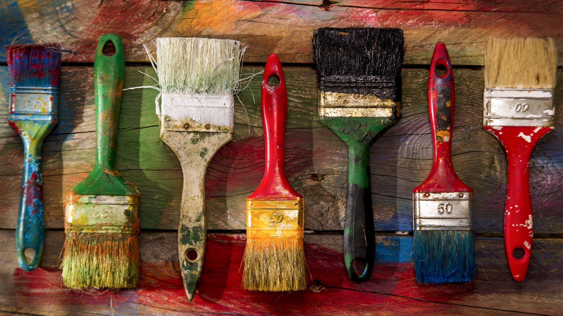 Assortment of used paintbrushes on a colorful wooden surface HD Wallpaper