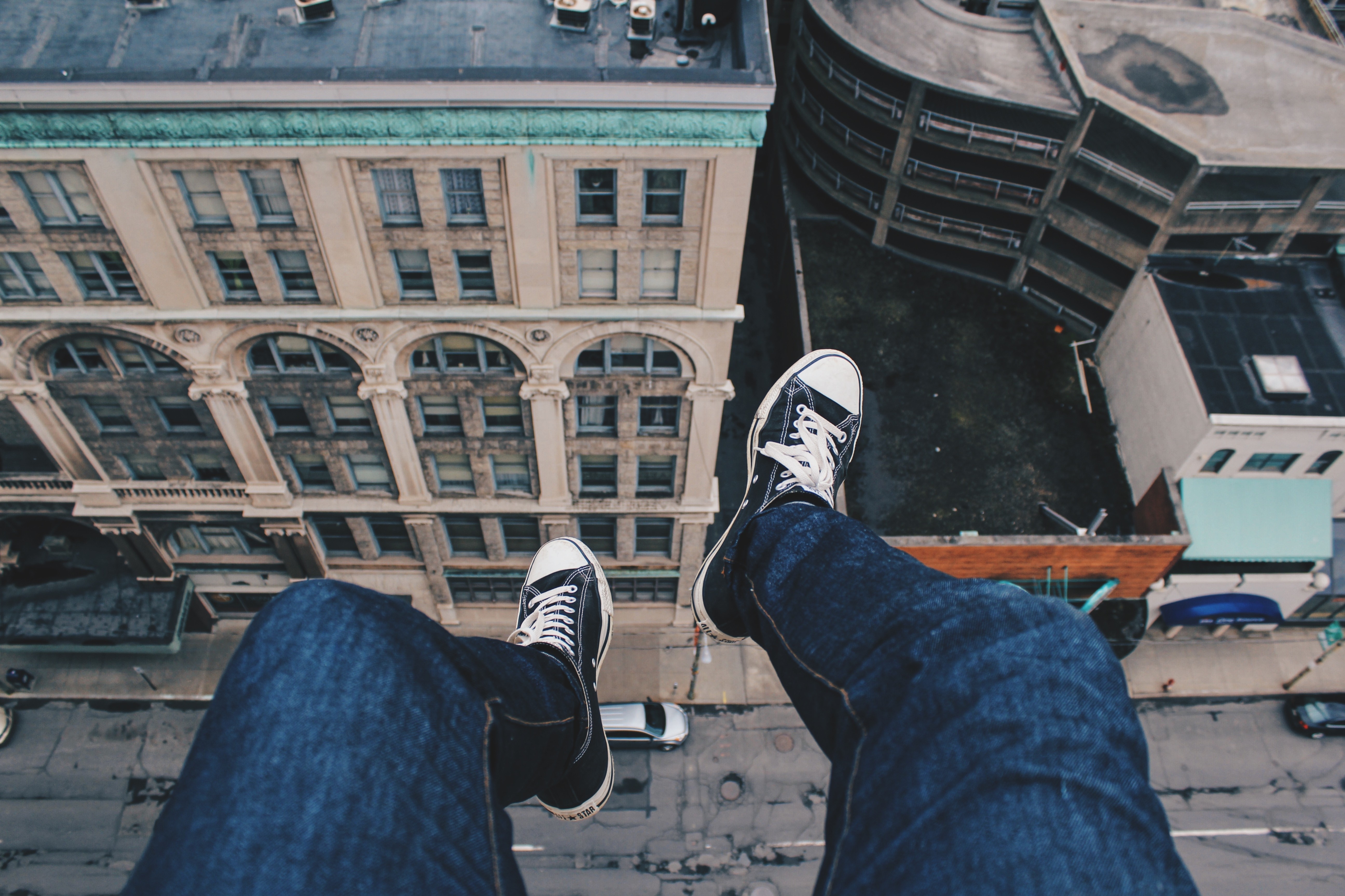 Person sitting on edge of building overlooking city HD Wallpaper