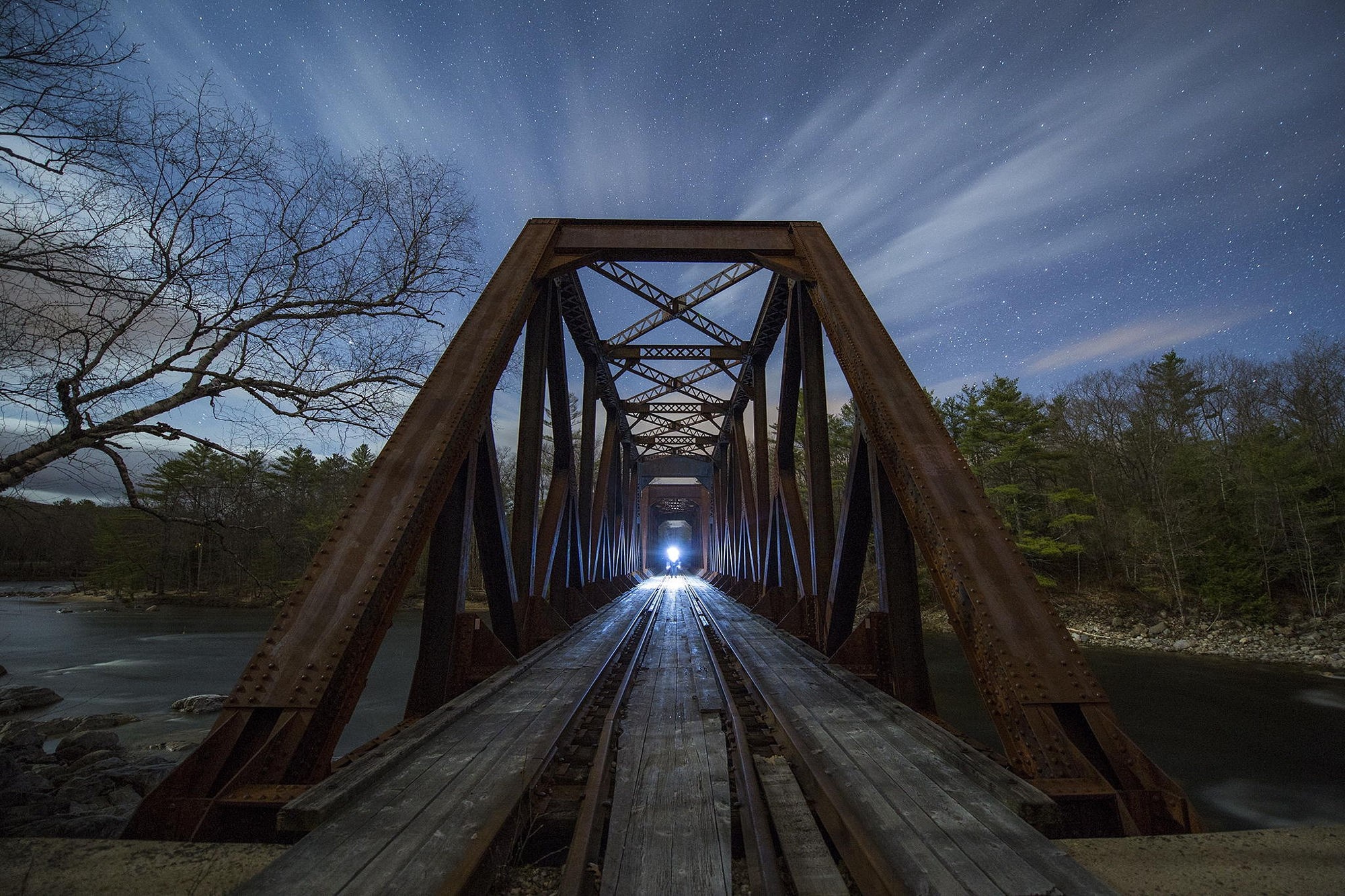 Rusty train bridge over a river at night under stars HD Wallpaper