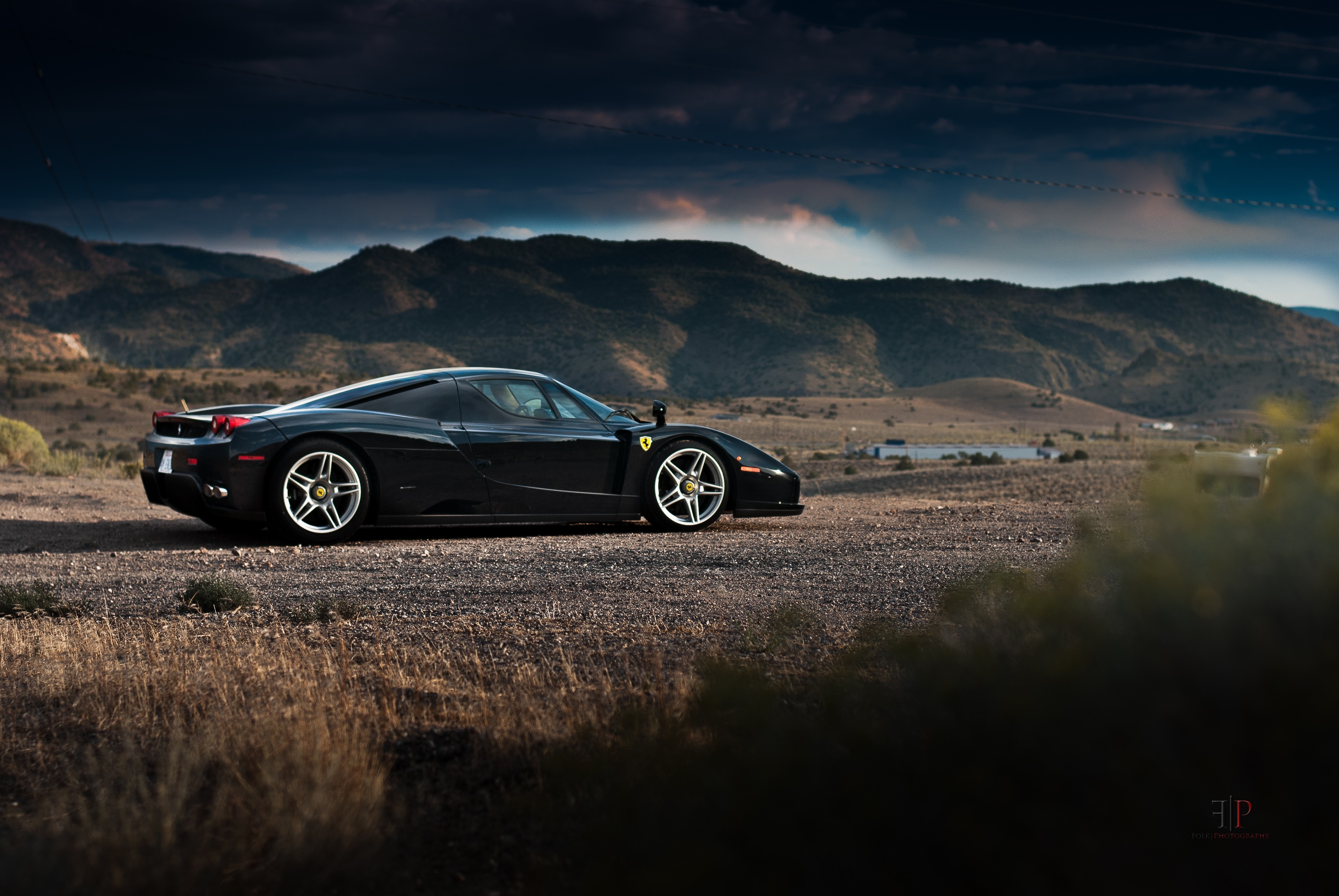 Black Ferrari Enzo parked on a dirt road with mountains HD Wallpaper