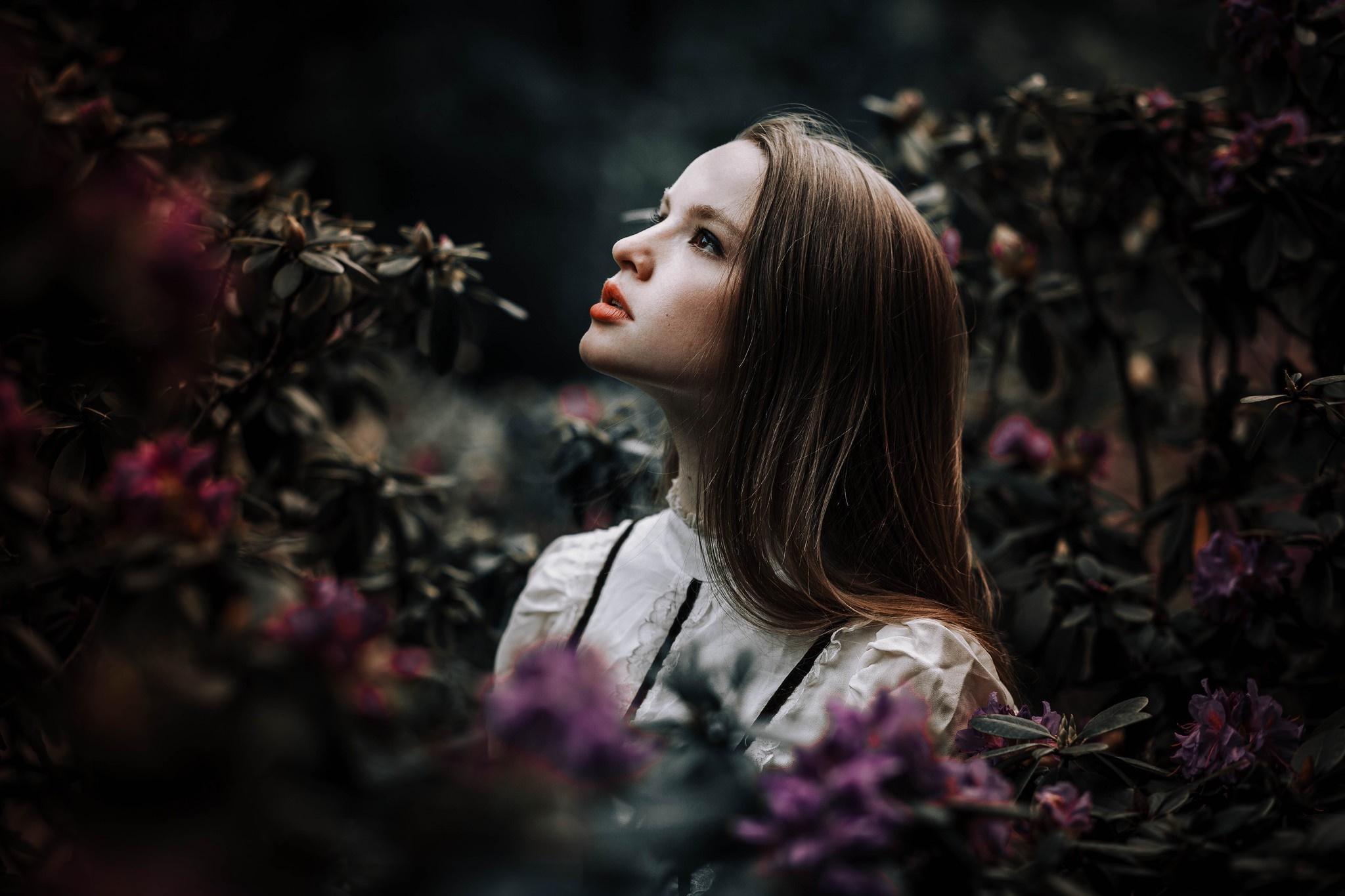 Woman in white dress surrounded by dark foliage and purple flowers HD Wallpaper