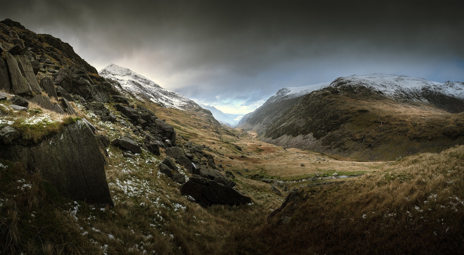 Panoramic view of a snow-dusted mountain valley under dramatic clouds HD Wallpaper
