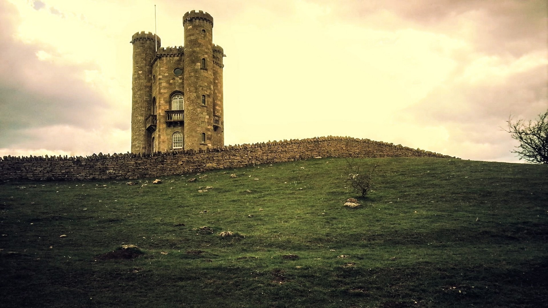 Castle tower on a grassy hill with stone wall HD Wallpaper