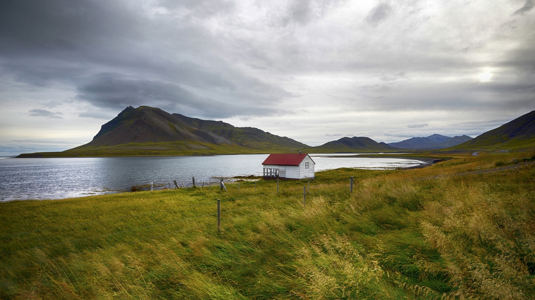Small white house with red roof by a bay with mountains HD Wallpaper