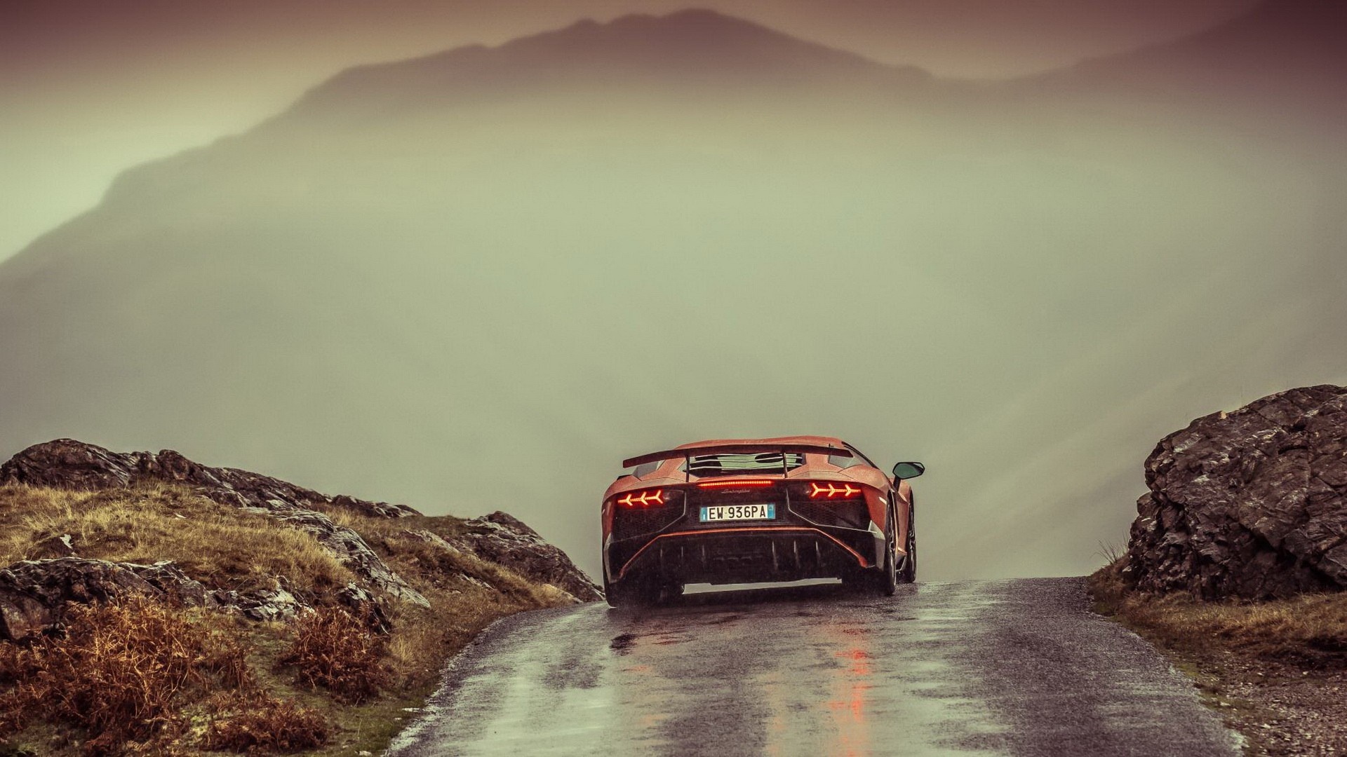 Orange Lamborghini Aventador driving on a wet mountain road HD Wallpaper