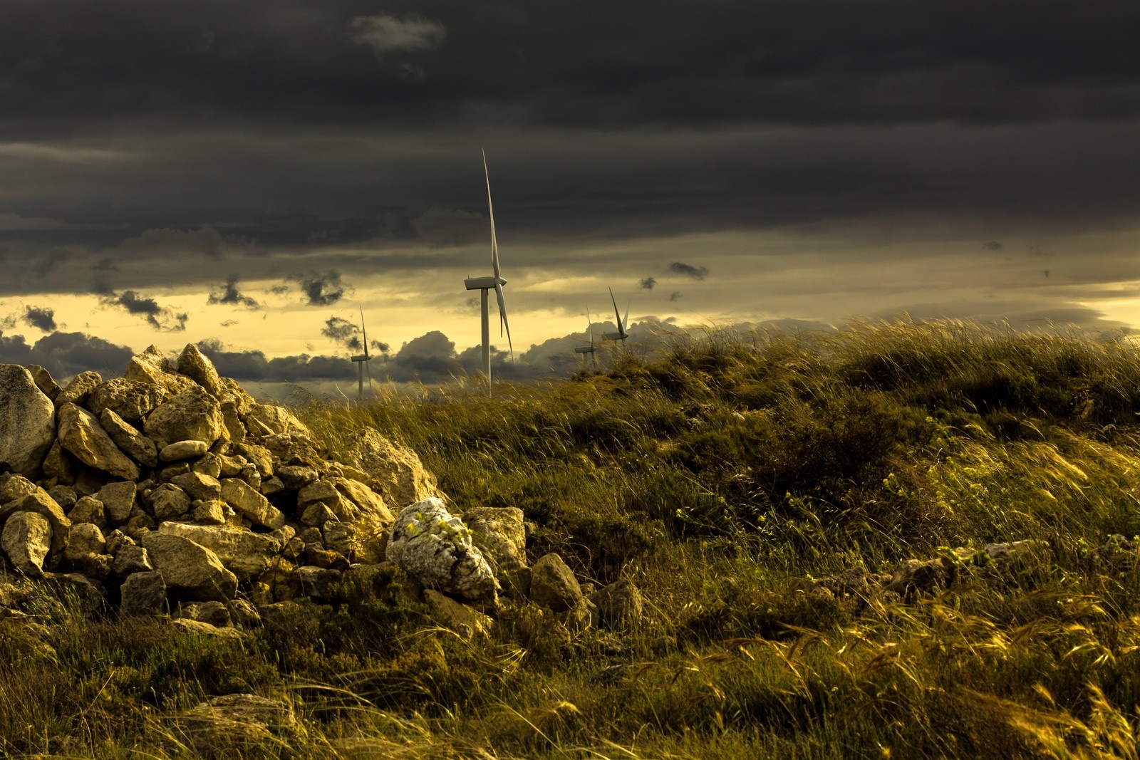 Wind turbines on a grassy hill under stormy clouds HD Wallpaper