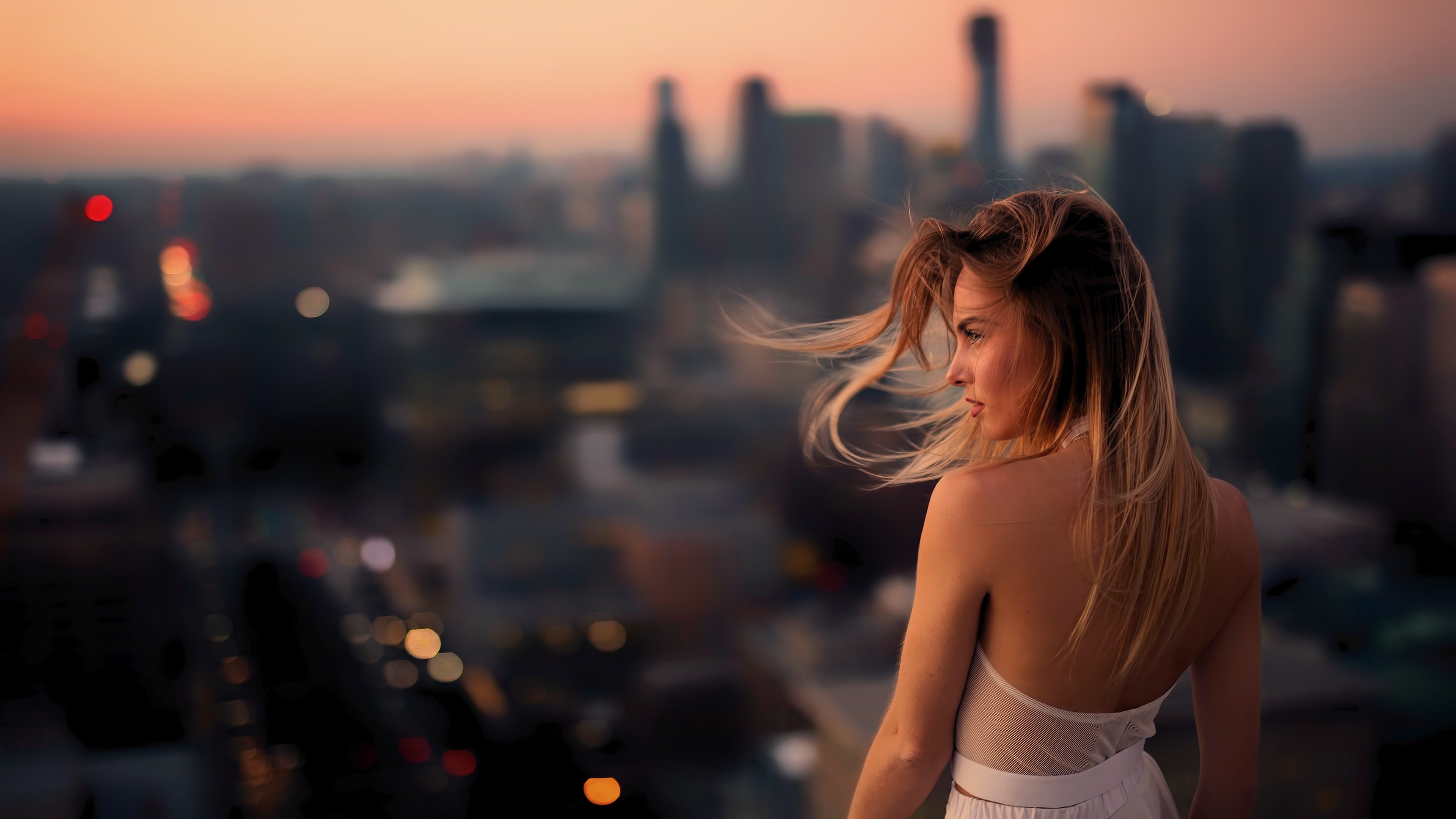 Woman with windblown hair overlooking city at dusk HD Wallpaper