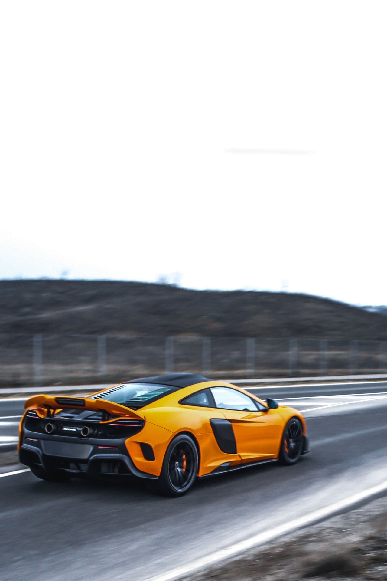 Orange McLaren 675LT driving on a highway HD Wallpaper