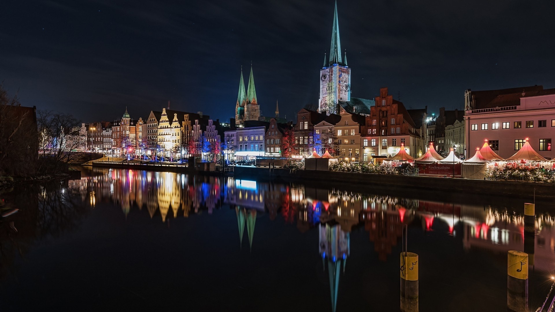 Cityscape at night with river reflection and market stalls HD Wallpaper