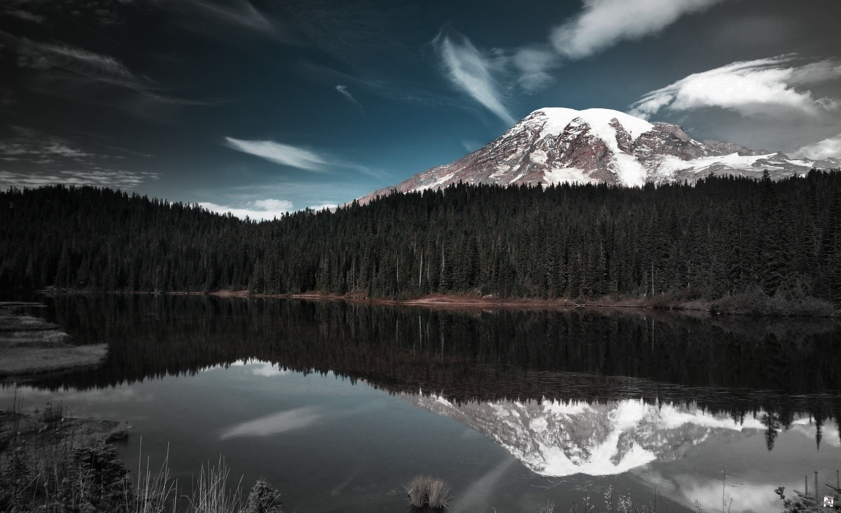 Snow-capped mountain reflected in a dark lake with pine forest HD Wallpaper