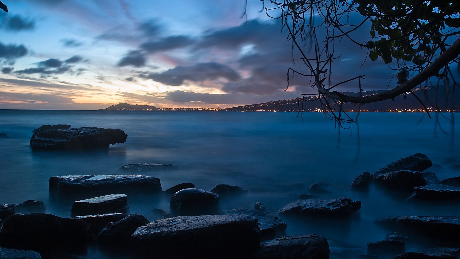 Ocean at Dusk with Rocks and Distant City Lights HD Wallpaper
