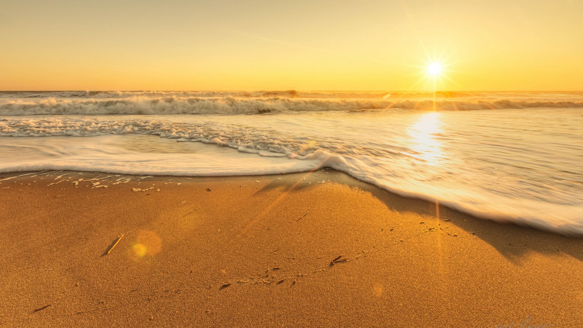 Sunset over a sandy beach with ocean waves HD Wallpaper