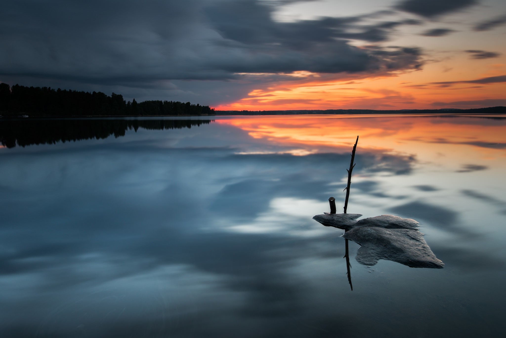 Sunset over a calm lake with a rock and stick HD Wallpaper