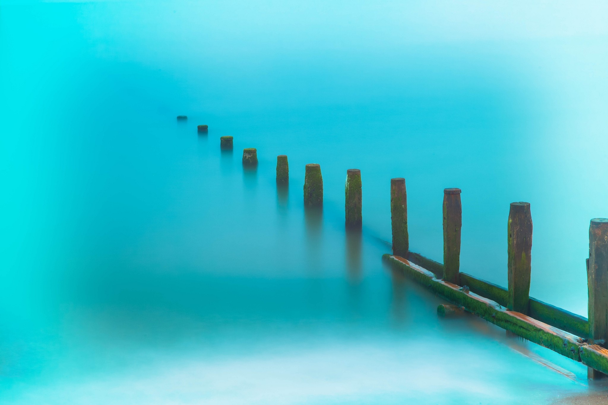 Wooden posts in the ocean with blue water HD Wallpaper