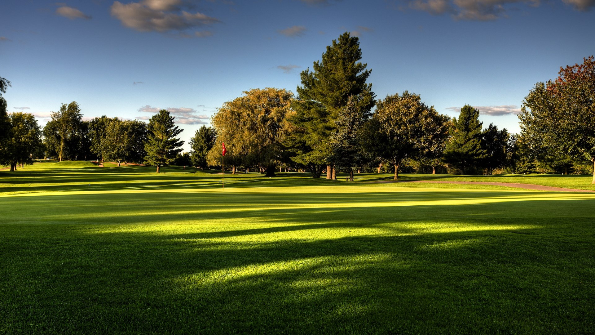 Golf course with trees and a red flag HD Wallpaper
