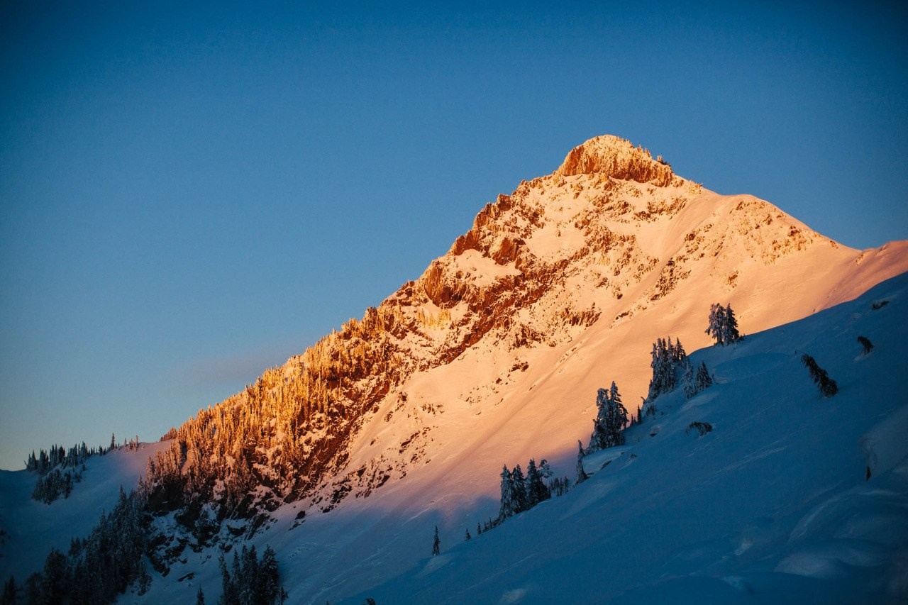 Snowy mountain peak illuminated by golden sunlight HD Wallpaper