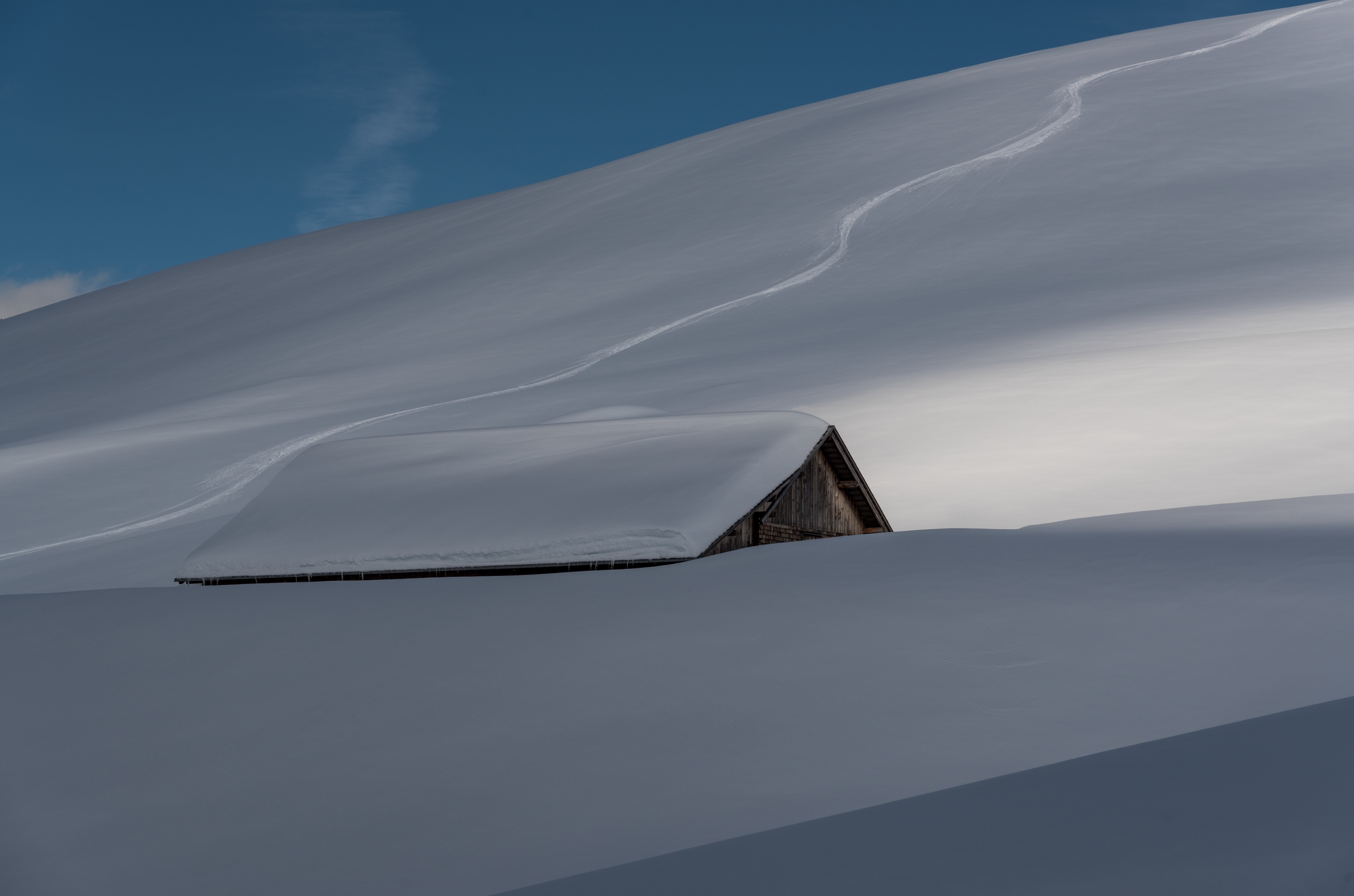 Wooden hut covered in snow with ski tracks on a mountain HD Wallpaper
