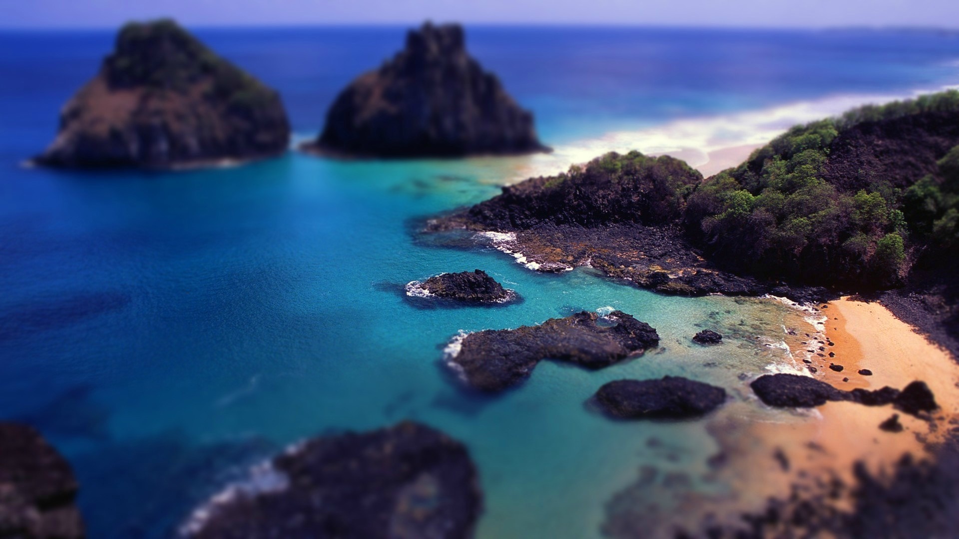 Tilt shift view of rocky islands and a sandy beach in the ocean HD Wallpaper