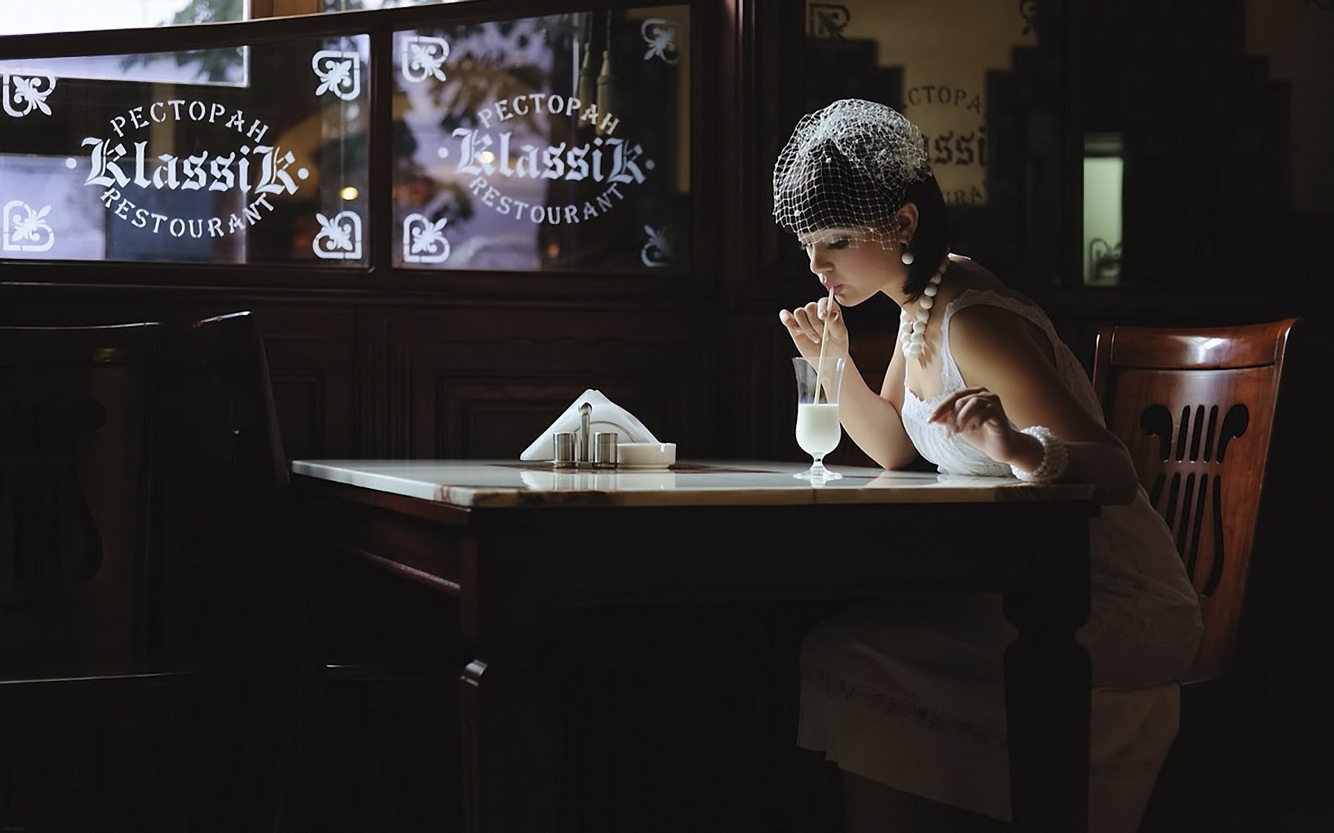Woman in vintage attire drinking from a glass in a restaurant HD Wallpaper