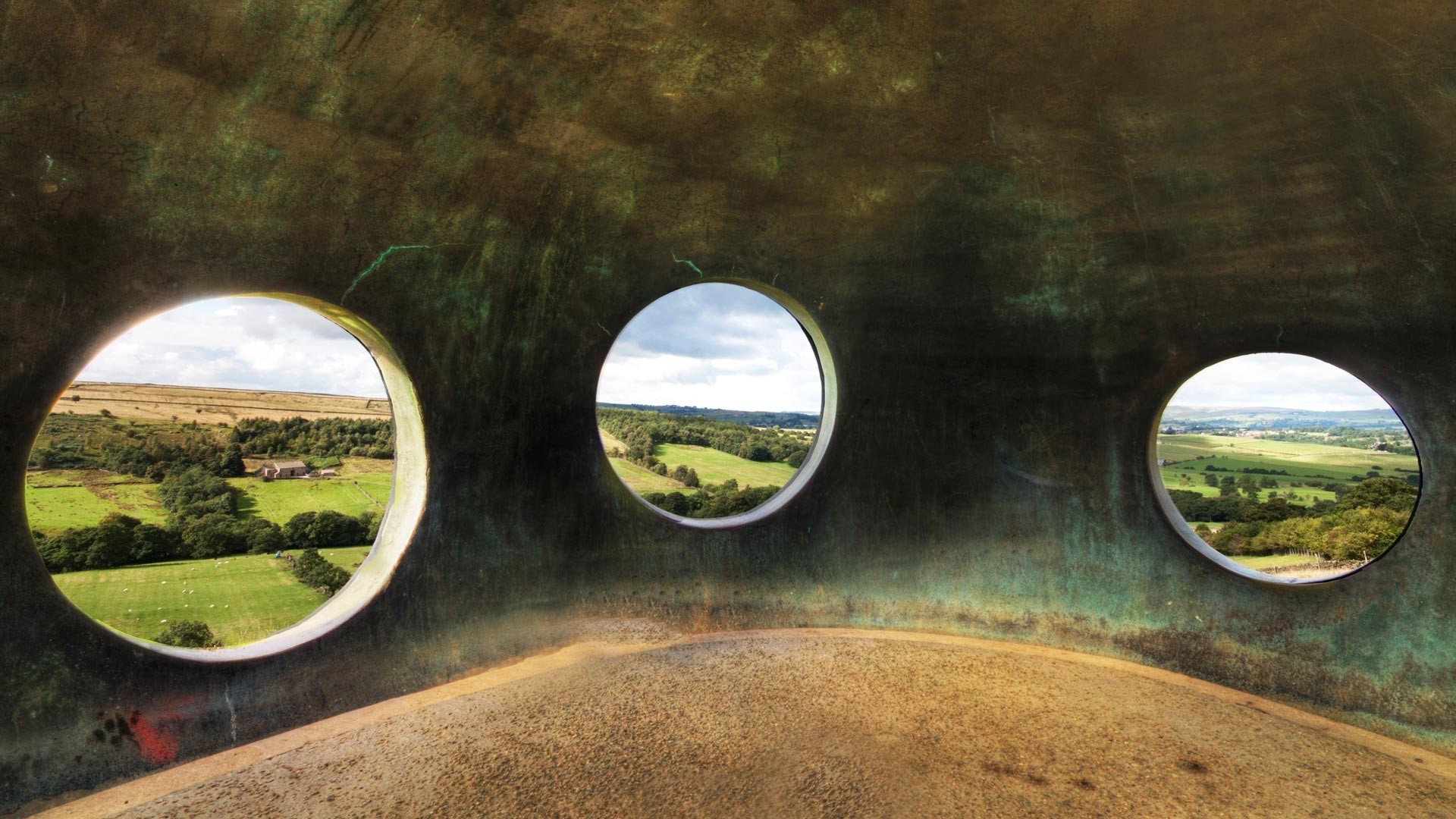 View of a rural landscape through circular openings in a structure HD Wallpaper