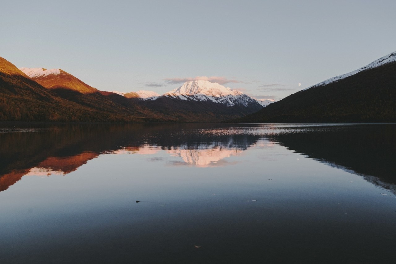 Snow-capped mountains reflected in a calm lake at sunrise HD Wallpaper