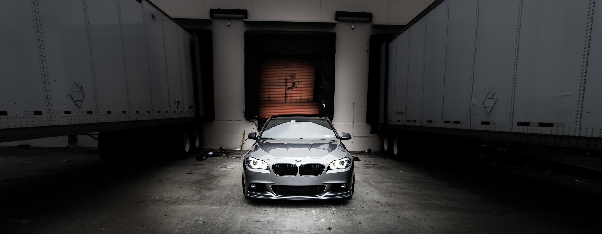 Gray BMW 5 Series Sedan parked between two trailers HD Wallpaper