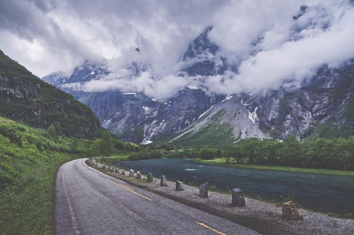 Road alongside a river in a mountainous valley with clouds HD Wallpaper