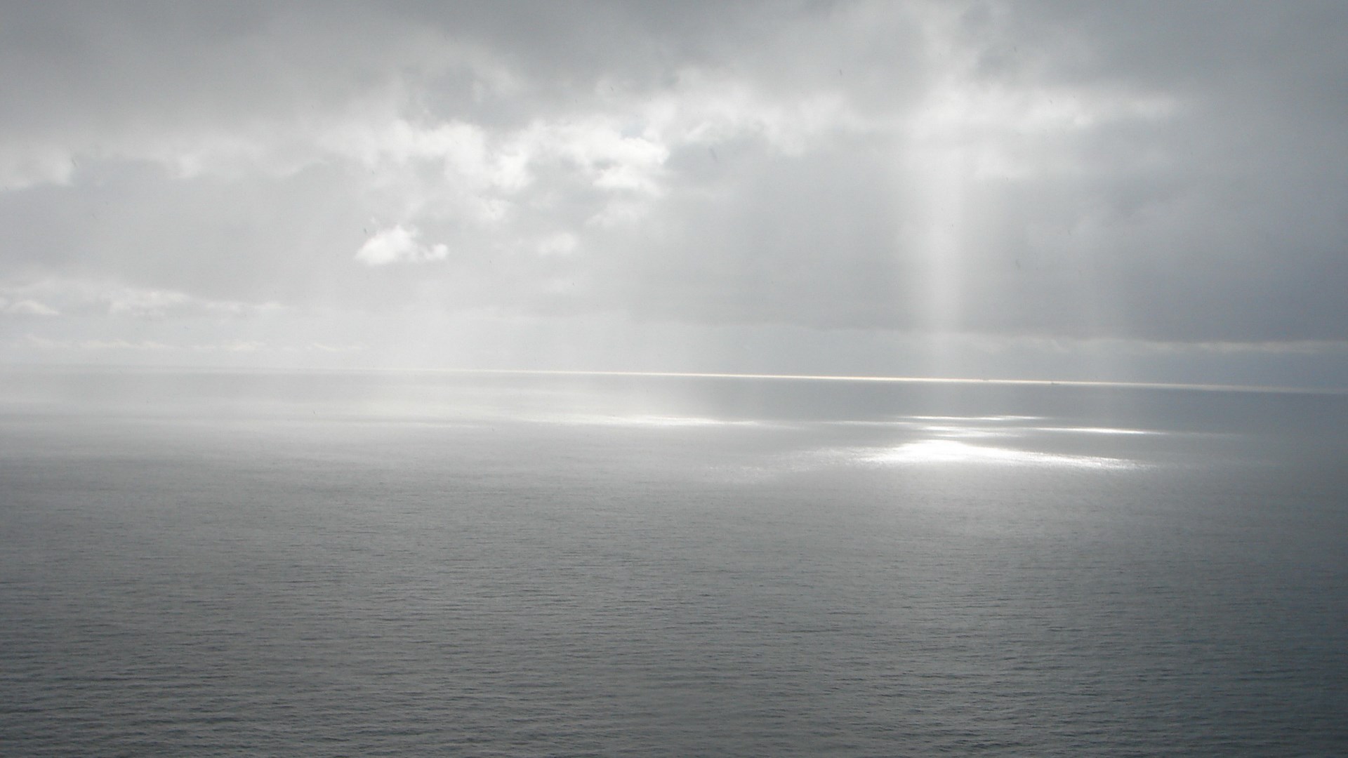 Sunlight beams through clouds onto a calm ocean HD Wallpaper