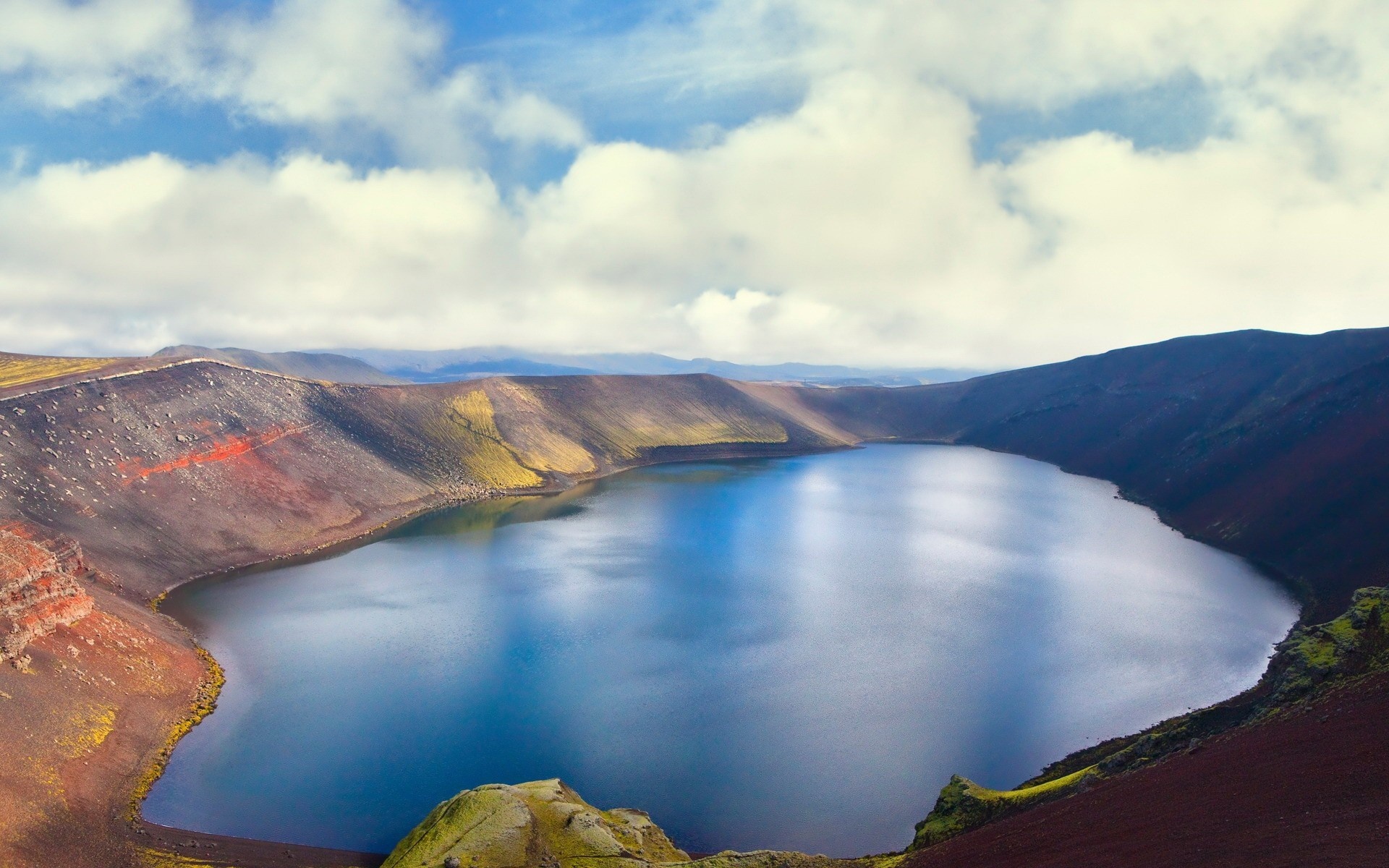 Crater lake with colorful volcanic slopes under a cloudy sky HD Wallpaper