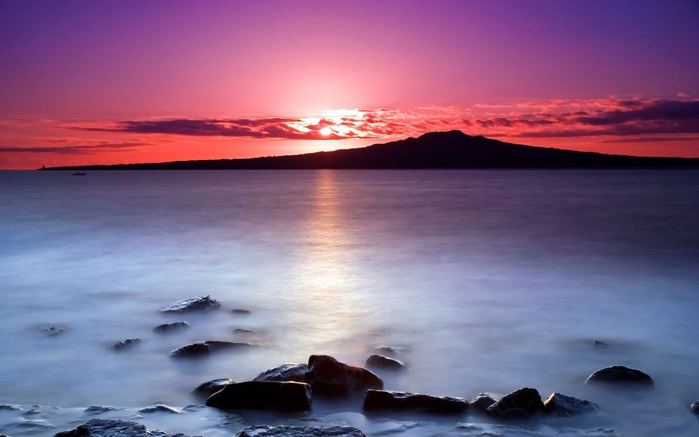 Sunset over the sea with a distant island and rocks HD Wallpaper