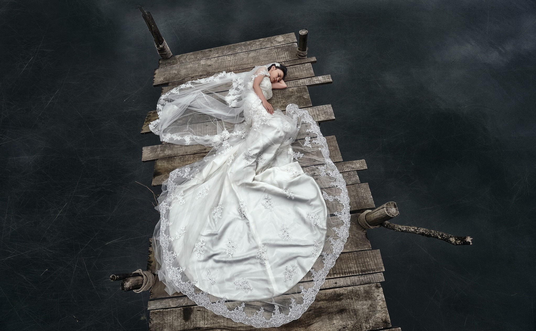 Bride in white dress lying on a wooden pier HD Wallpaper