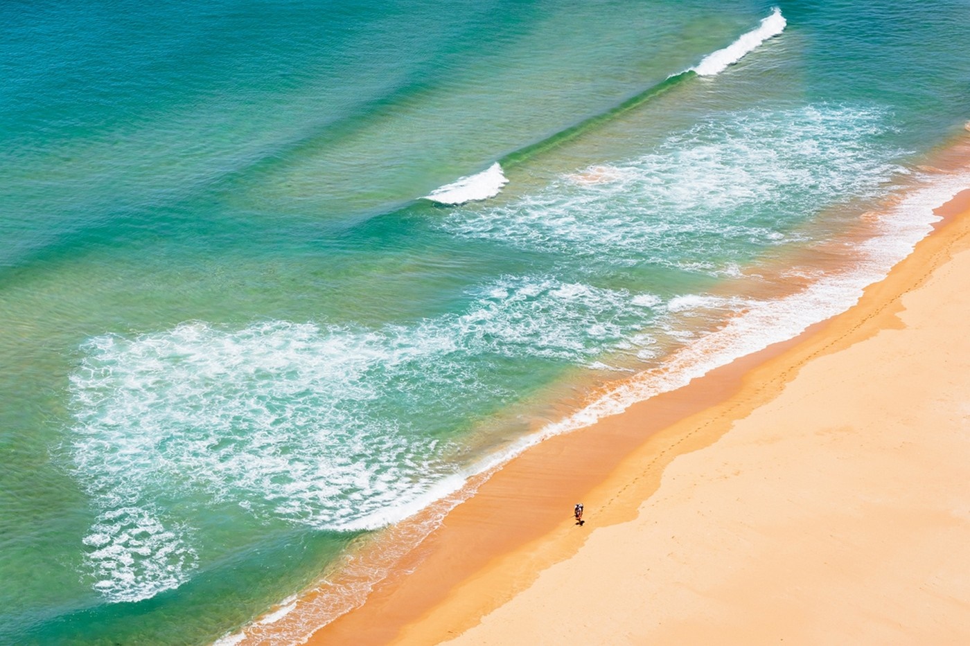 Two people walking on a sandy beach with turquoise ocean waves HD Wallpaper