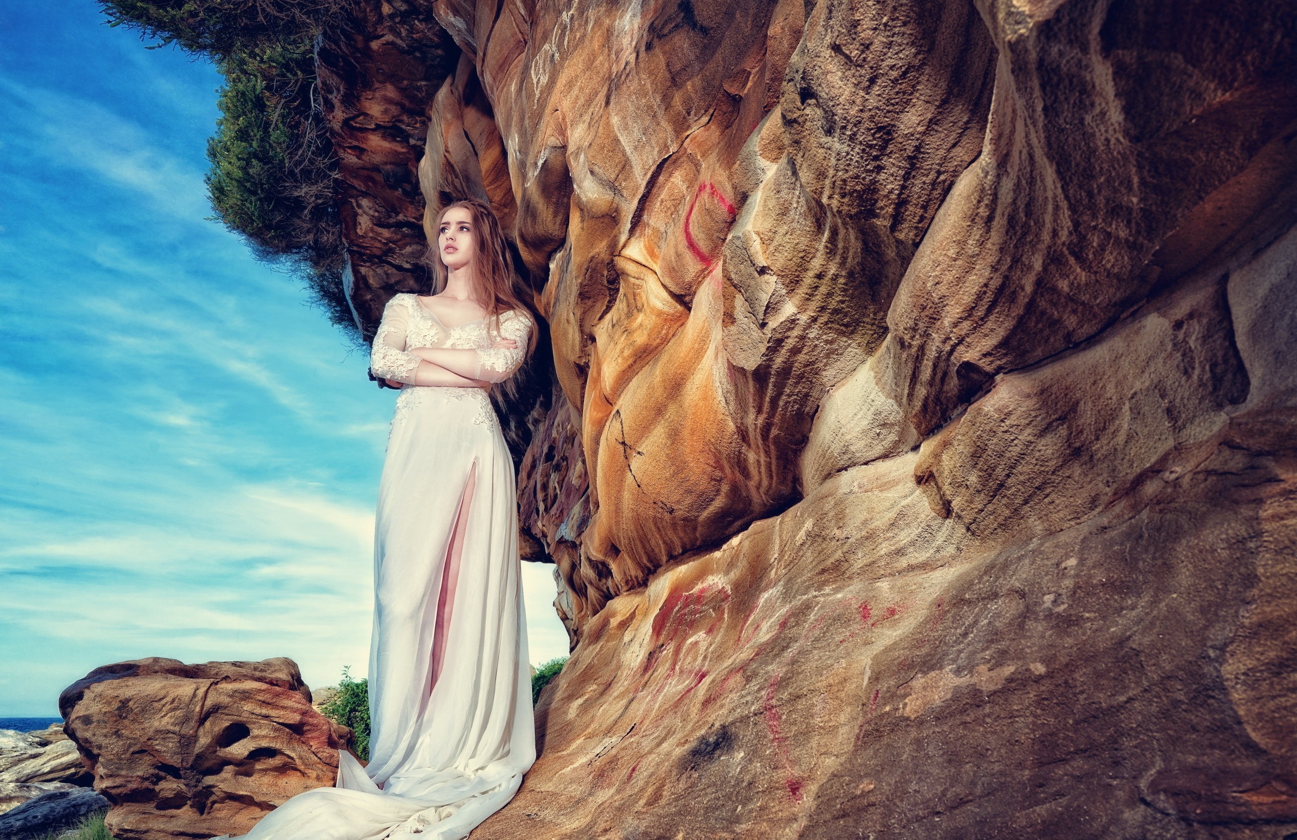 Woman in a white dress standing by a rock formation HD Wallpaper
