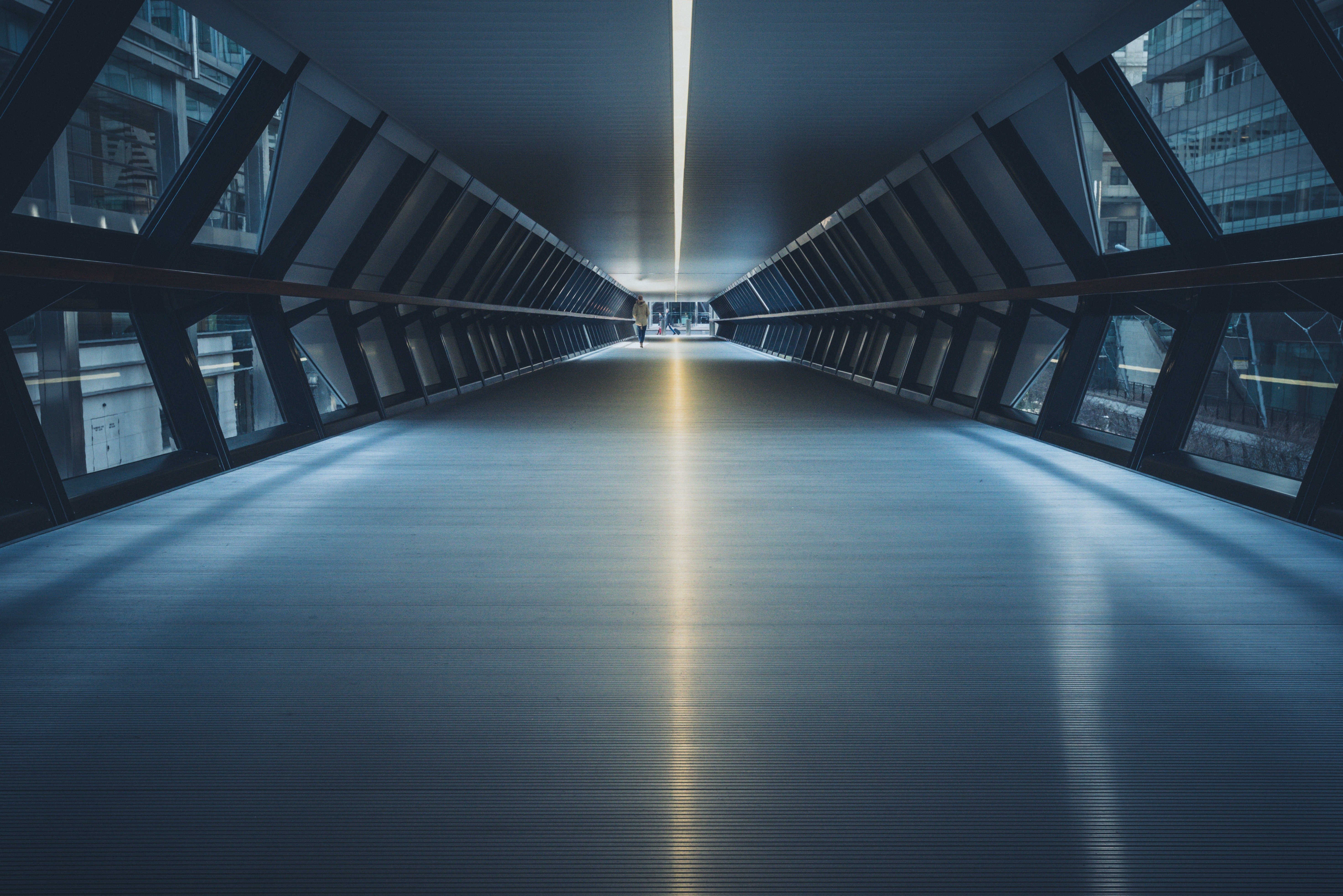 Modern glass and steel pedestrian tunnel with a lone figure HD Wallpaper