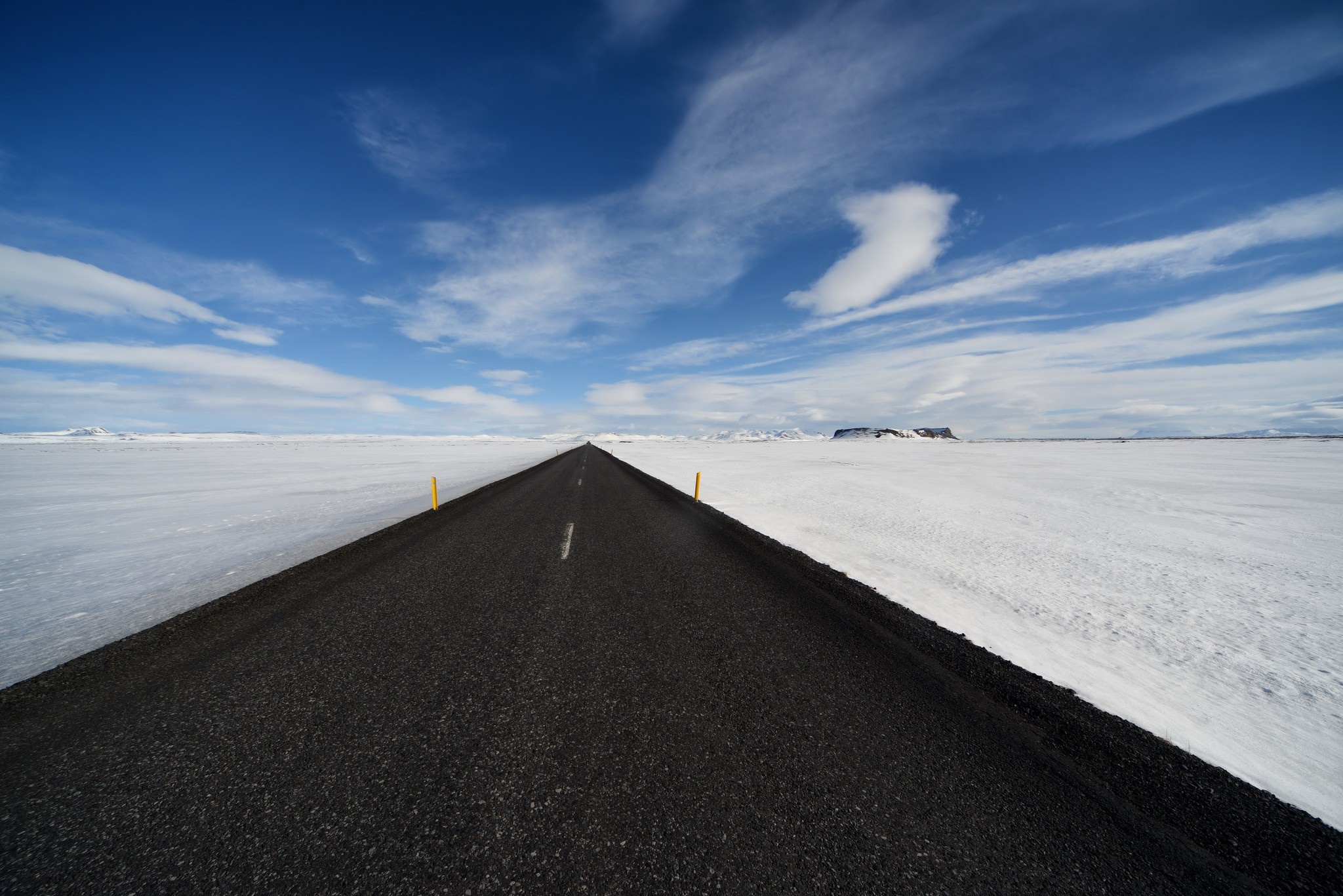 Asphalt road through a snowy landscape under a blue sky HD Wallpaper