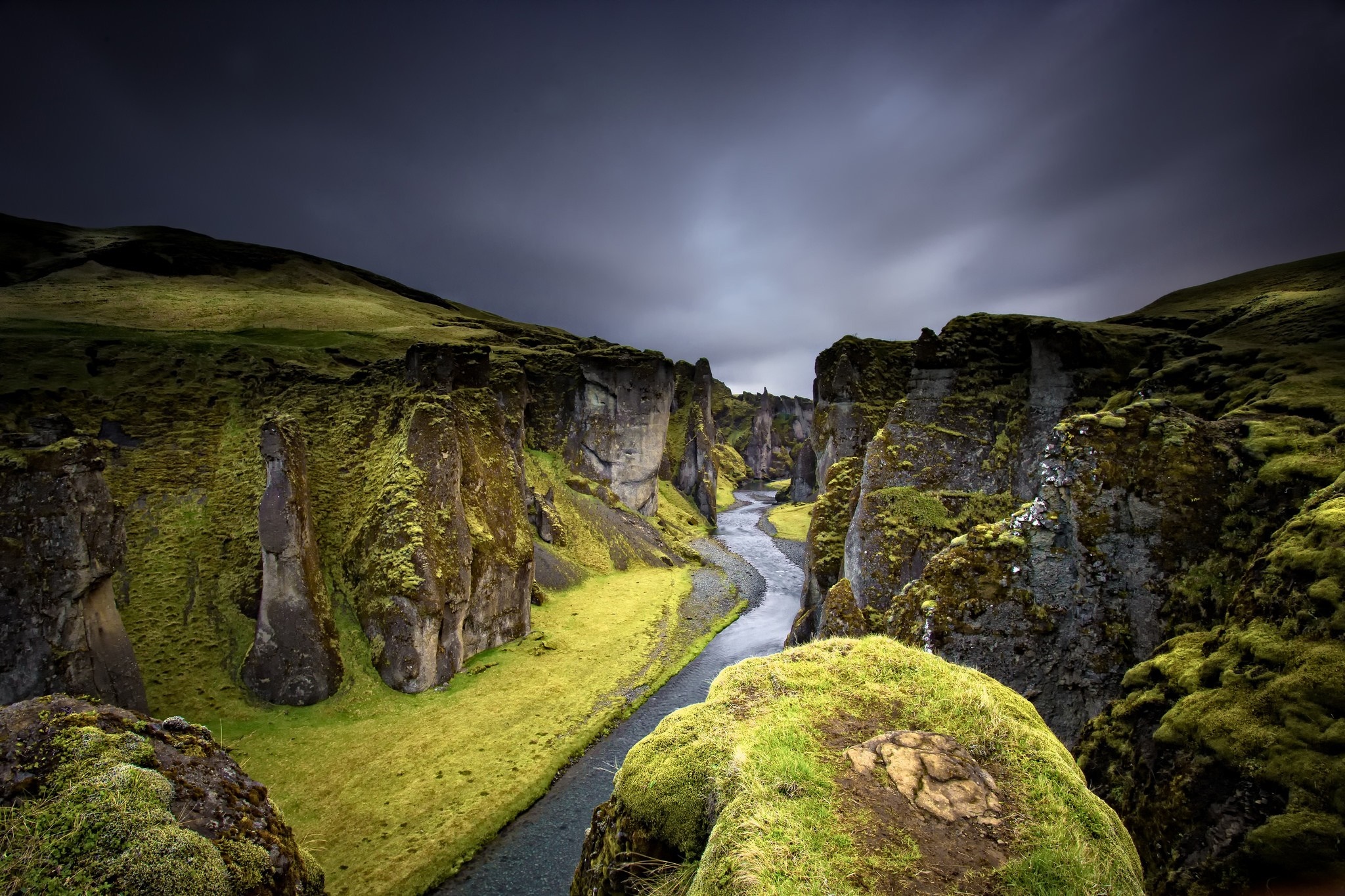 Moss-covered canyon with a winding river under a cloudy sky HD Wallpaper
