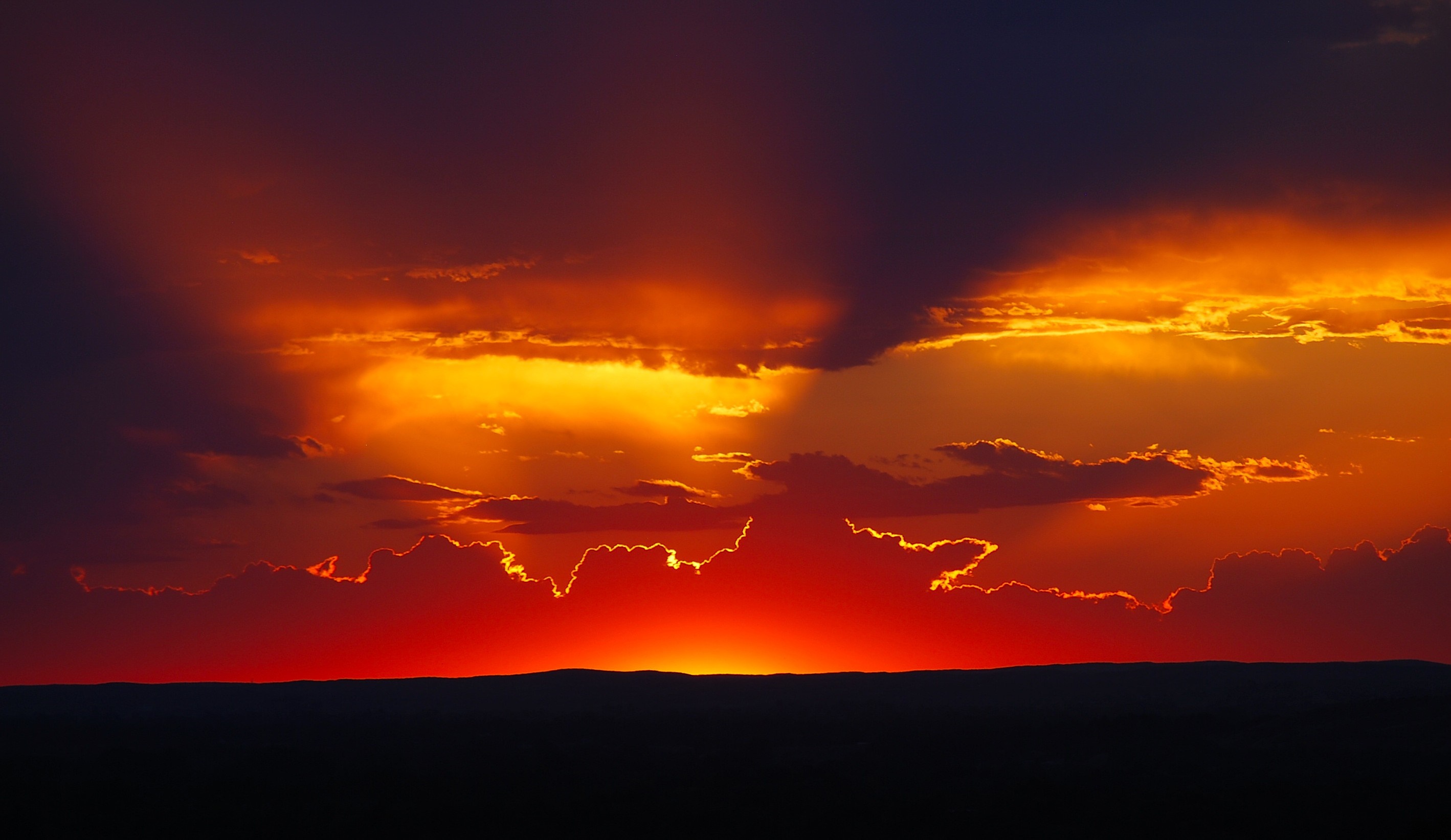 Dramatic sunset over a dark horizon with vibrant clouds HD Wallpaper