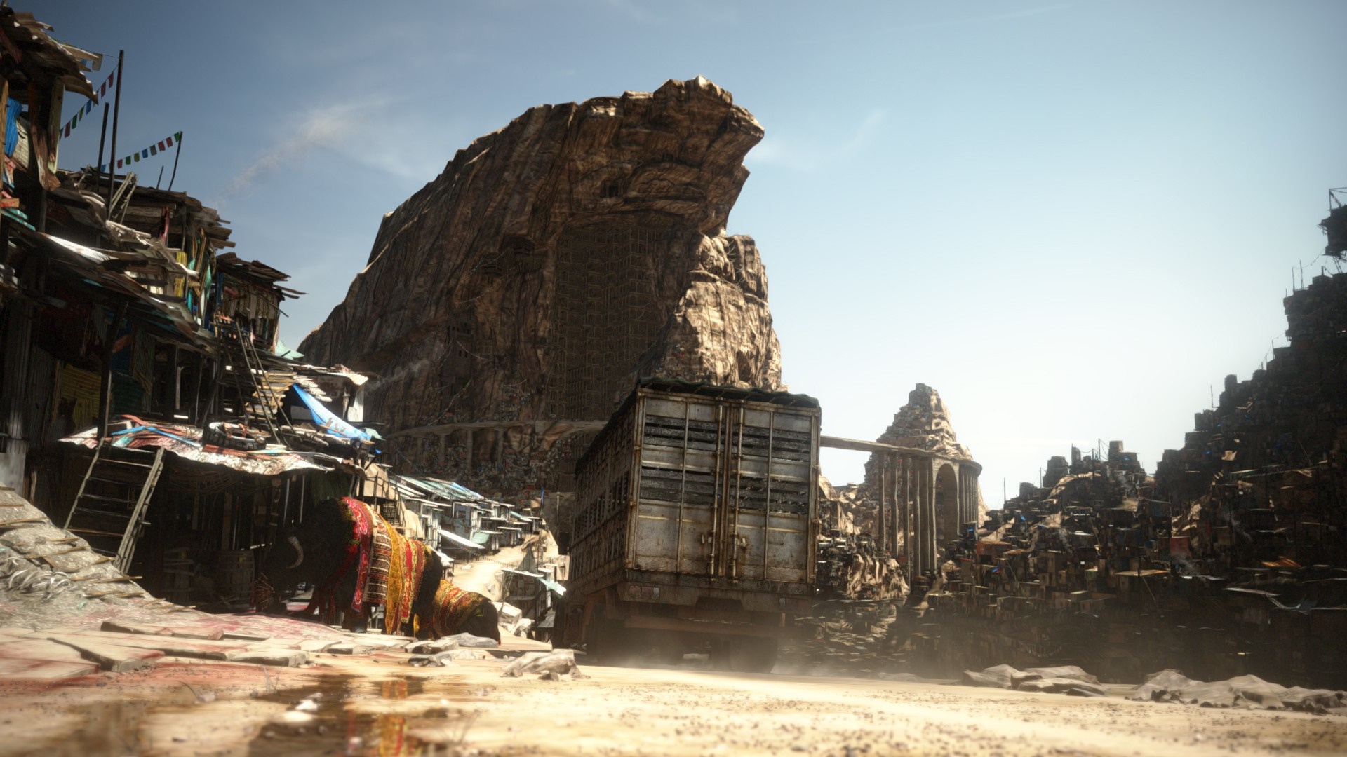 Post-apocalyptic settlement with a large truck and rocky mountains HD Wallpaper