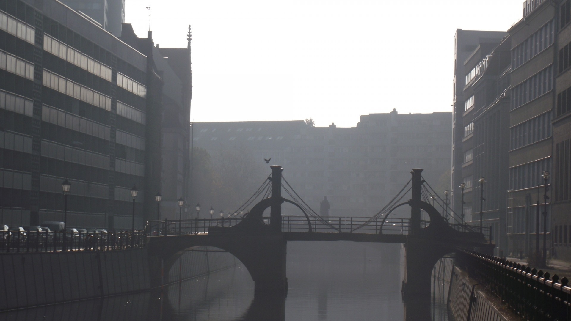 Misty bridge over a river in a city with buildings HD Wallpaper
