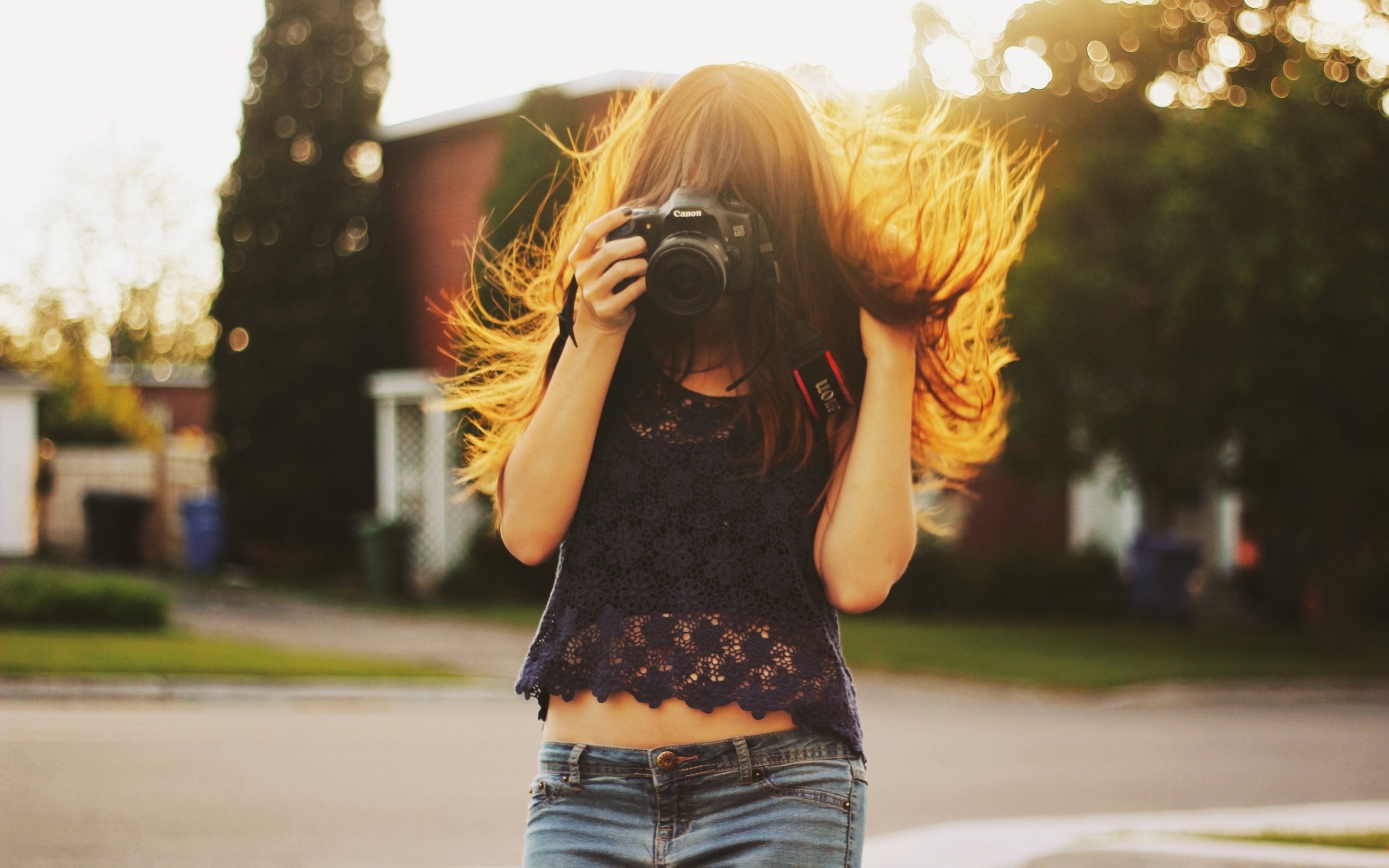 Woman holding a Canon camera with hair blowing in sunlight HD Wallpaper