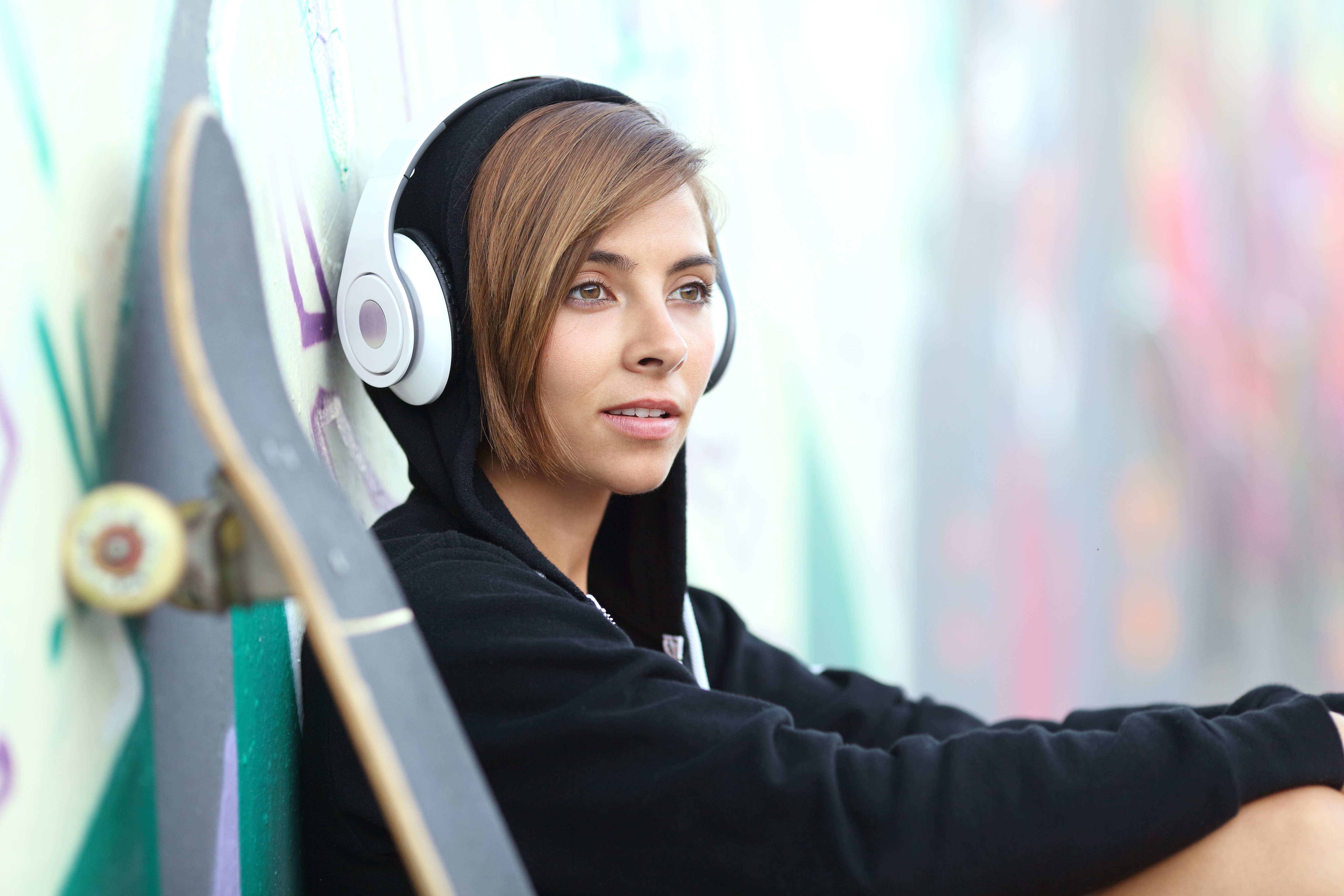 Young woman with headphones and skateboard near graffiti wall HD Wallpaper