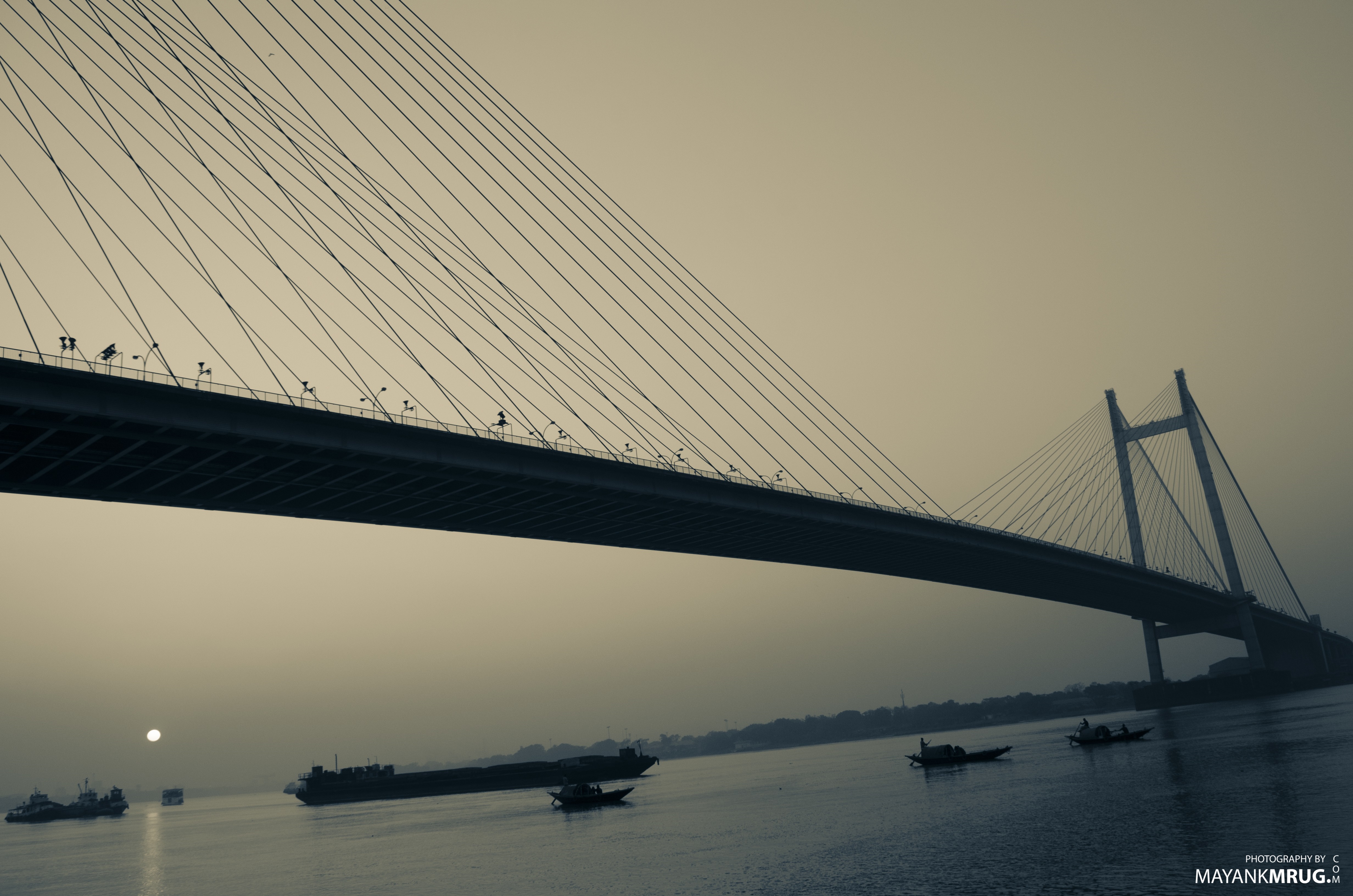 Cable-stayed bridge over a river at sunset with boats HD Wallpaper
