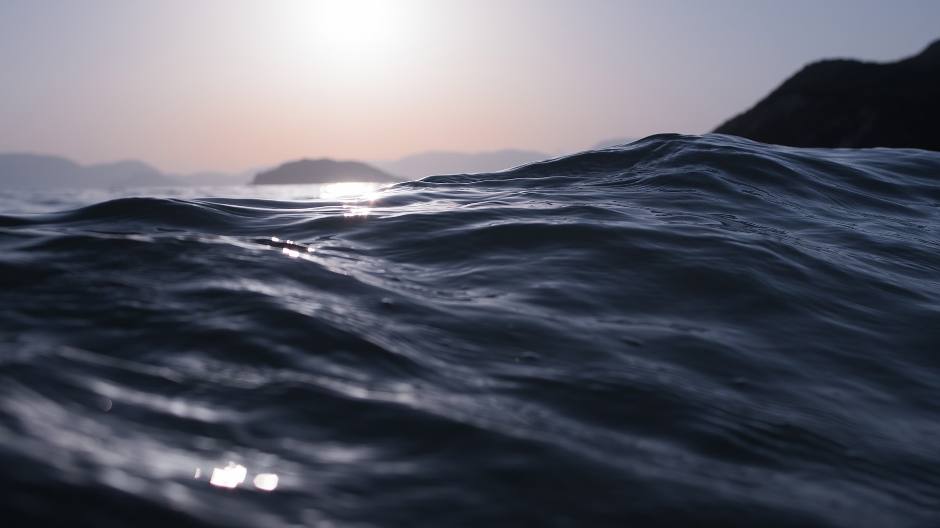 Close-up of ocean waves at sunset with mountains in the background HD Wallpaper