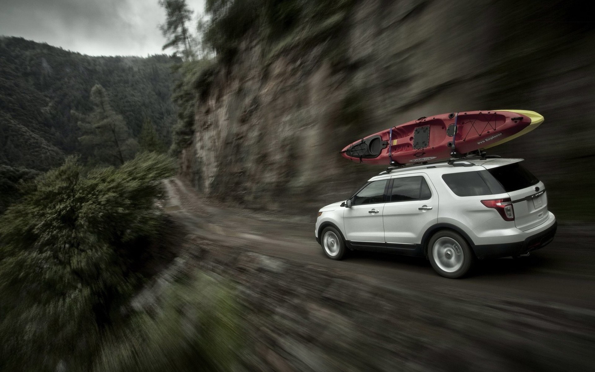 White SUV with Kayak on Roof Driving on Mountain Road HD Wallpaper