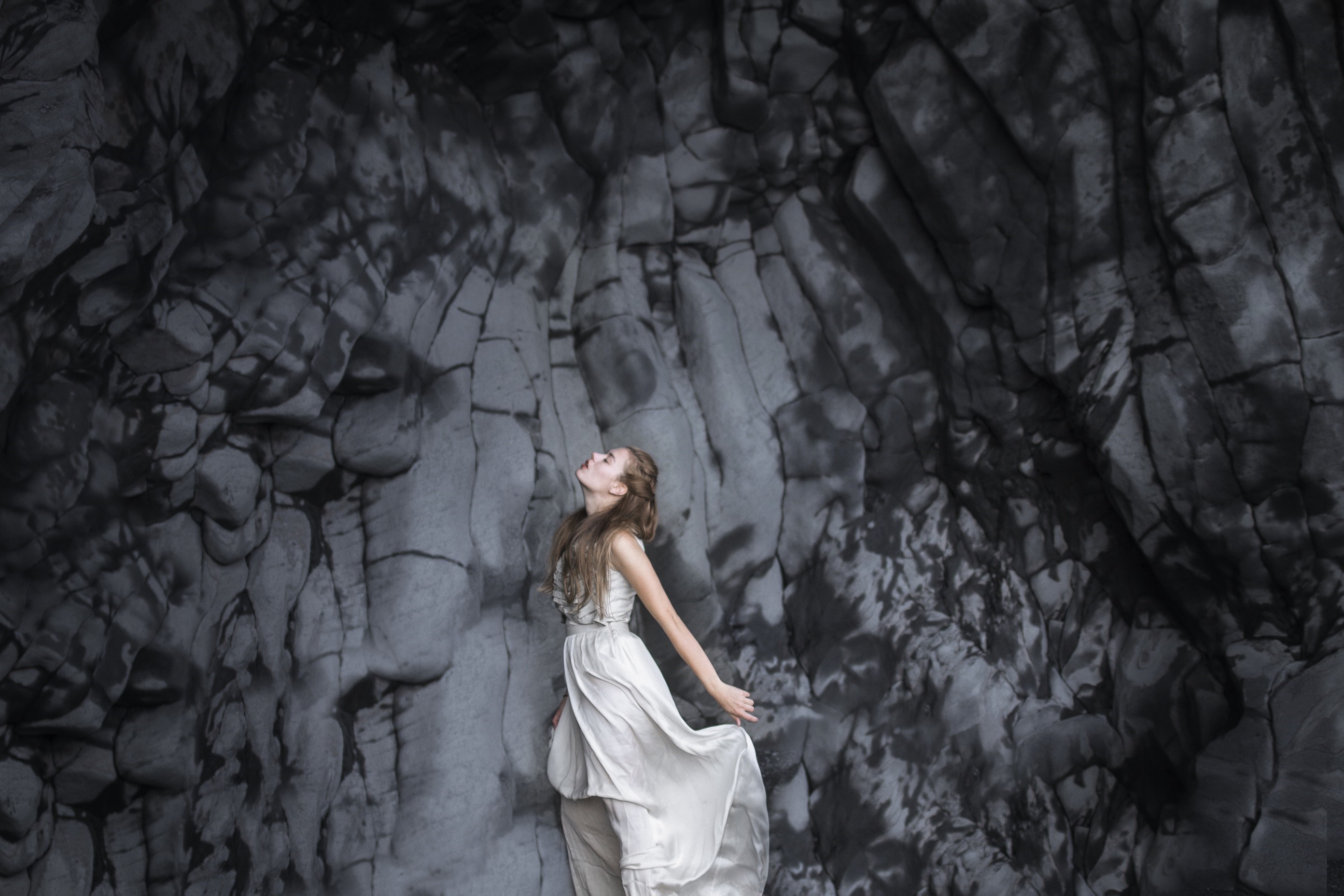 Woman in white dress against dark rock formation HD Wallpaper