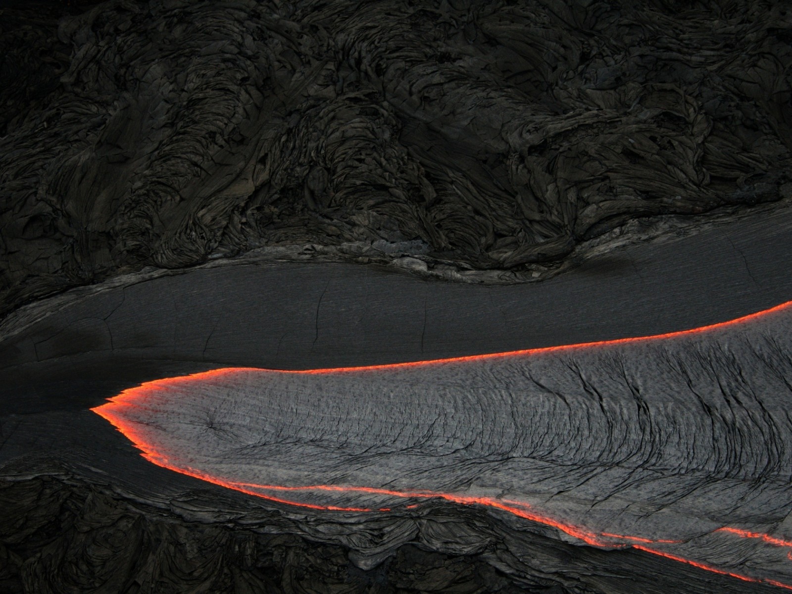 Molten lava flowing through dark volcanic rock formations HD Wallpaper