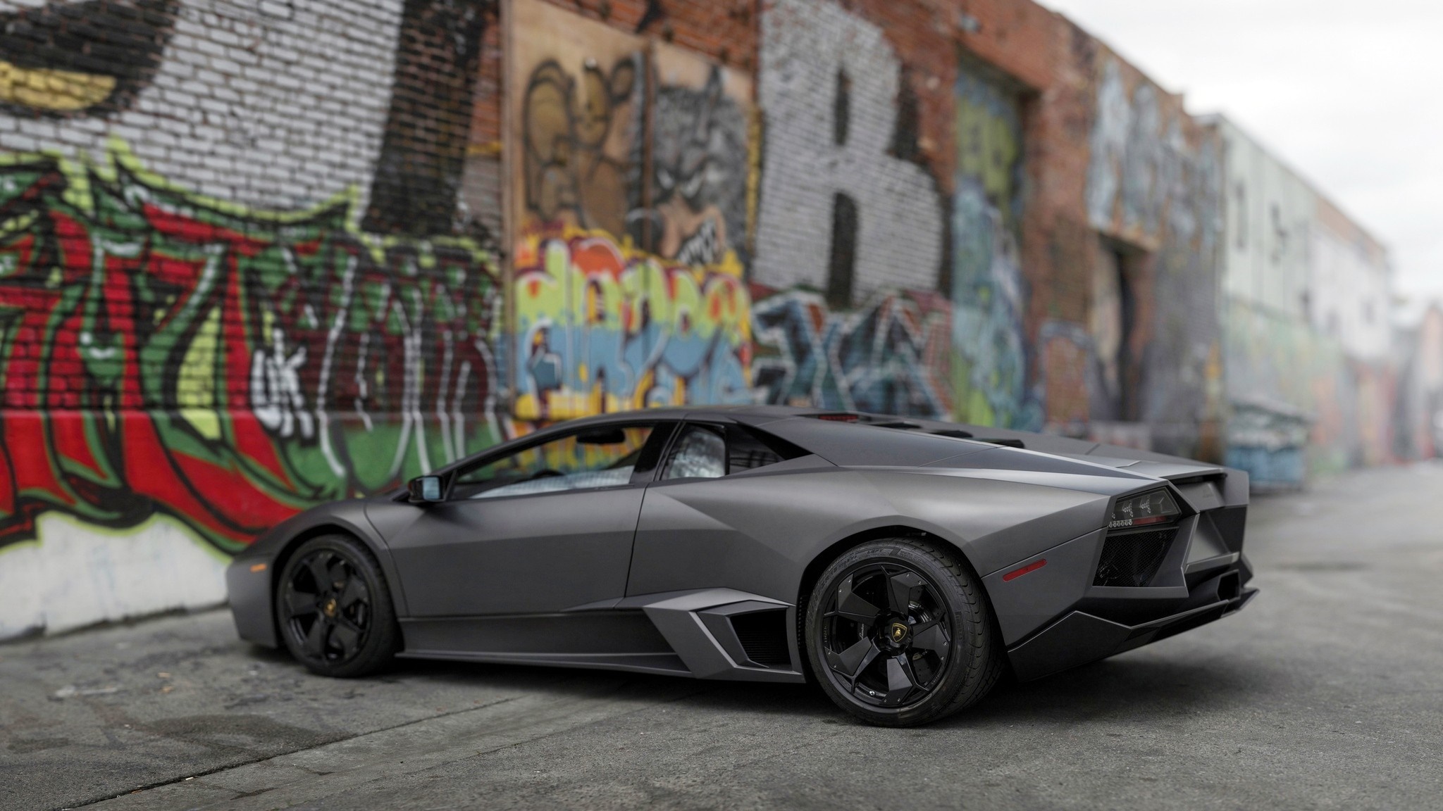 Matte gray Lamborghini Reventon parked against graffiti wall HD Wallpaper