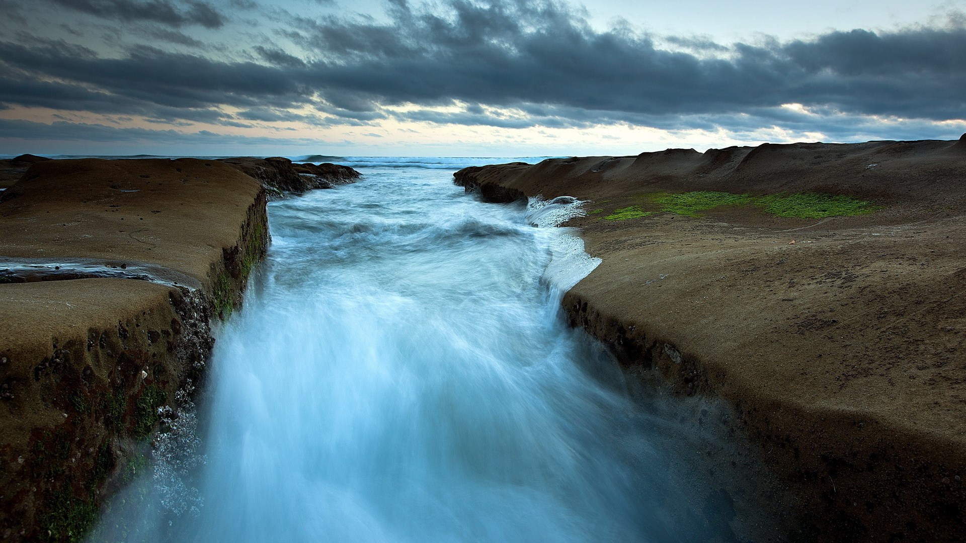 Ocean waves crashing against rocky shore at dusk HD Wallpaper