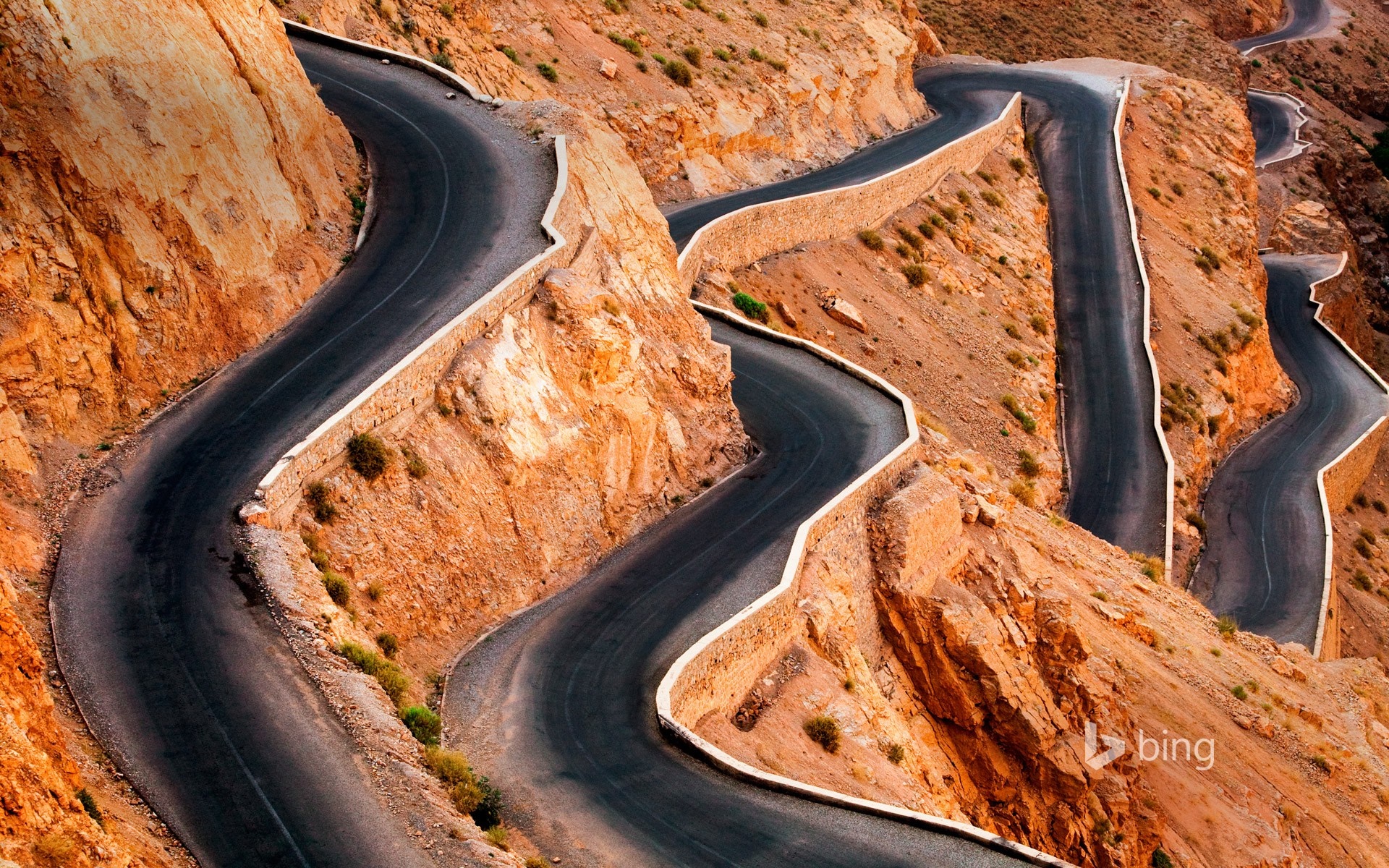 Winding mountain road carved into rocky terrain HD Wallpaper