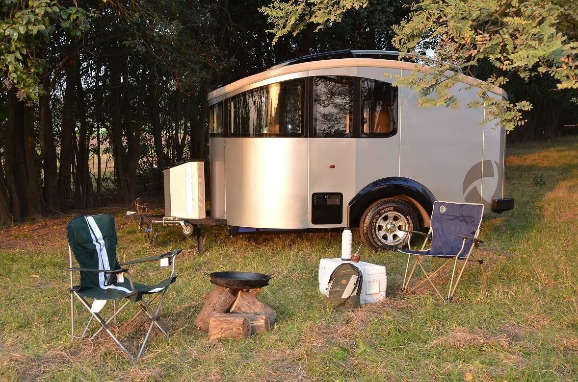 Camper trailer with chairs and campfire setup HD Wallpaper